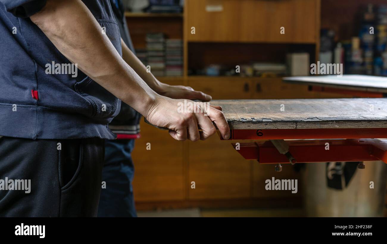 produzione serigrafica. stampa di immagini su magliette con metodo serigrafico in uno studio di design. focus fotografico selettivo di mani maschili. i lavoratori sono pronti a Foto Stock