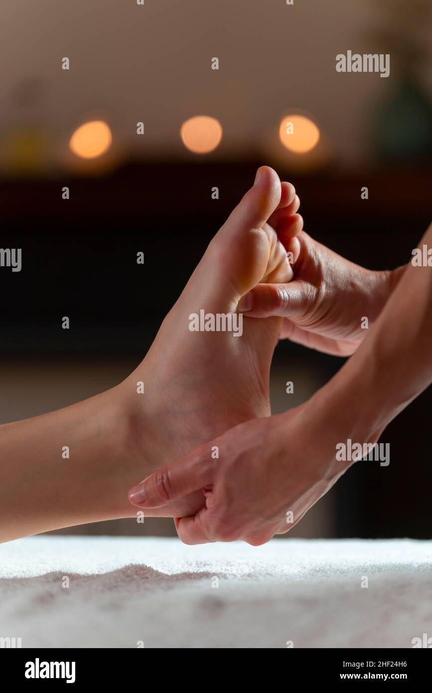 Massaggiatore che fa un massaggio ai piedi con candele sullo sfondo Foto Stock