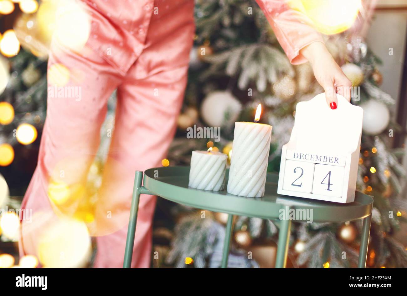 Giorno di Natale. Scatto ritagliato della donna in pajama flipping calendario in legno dal 24 al 25 dicembre di mattina, in piedi vicino al firtree decorato a casa, fe Foto Stock