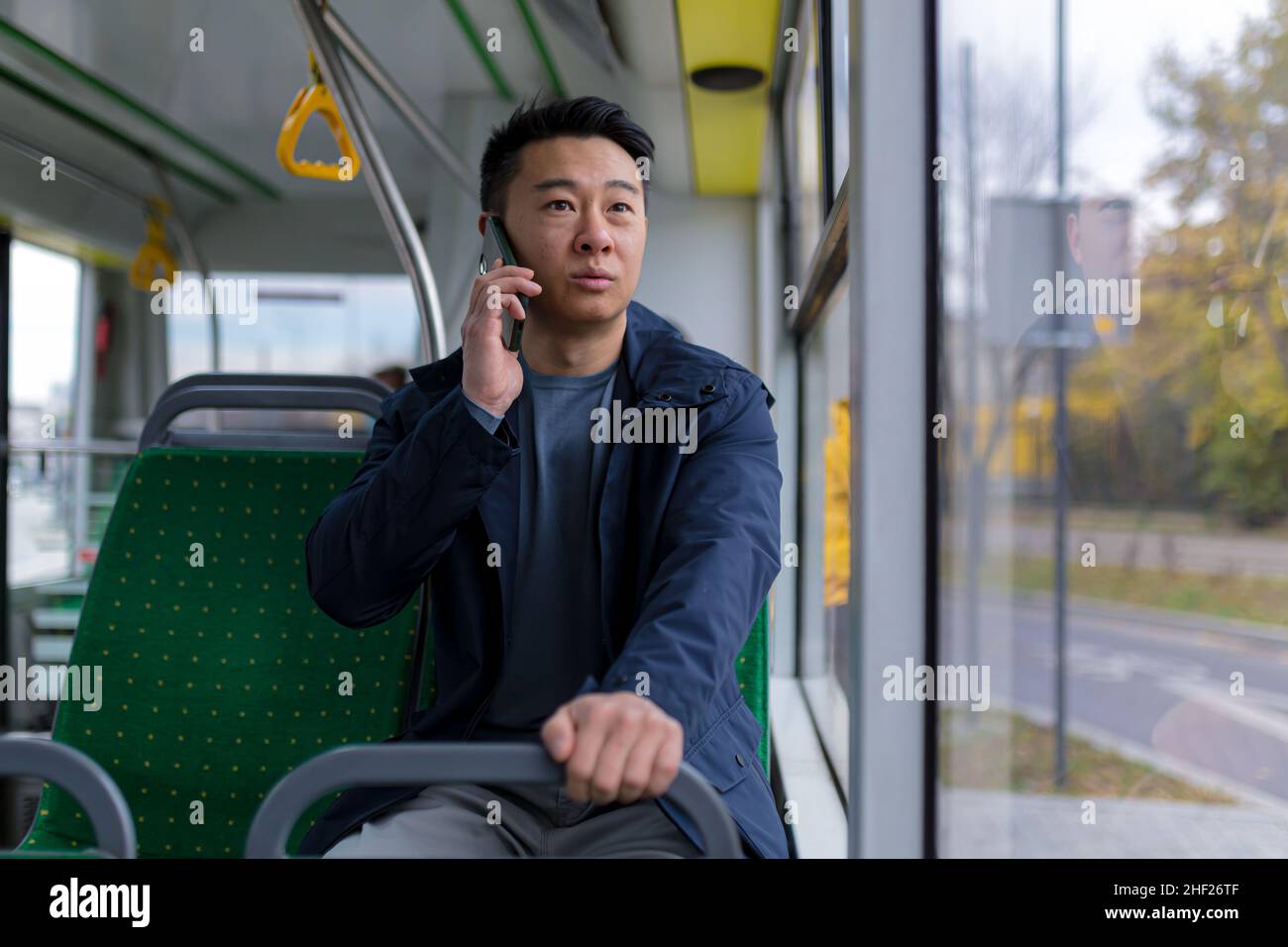 Uomo asiatico ansioso e spaventato, a bordo di un autobus pubblico, un passeggero che parla su un telefono cellulare Foto Stock