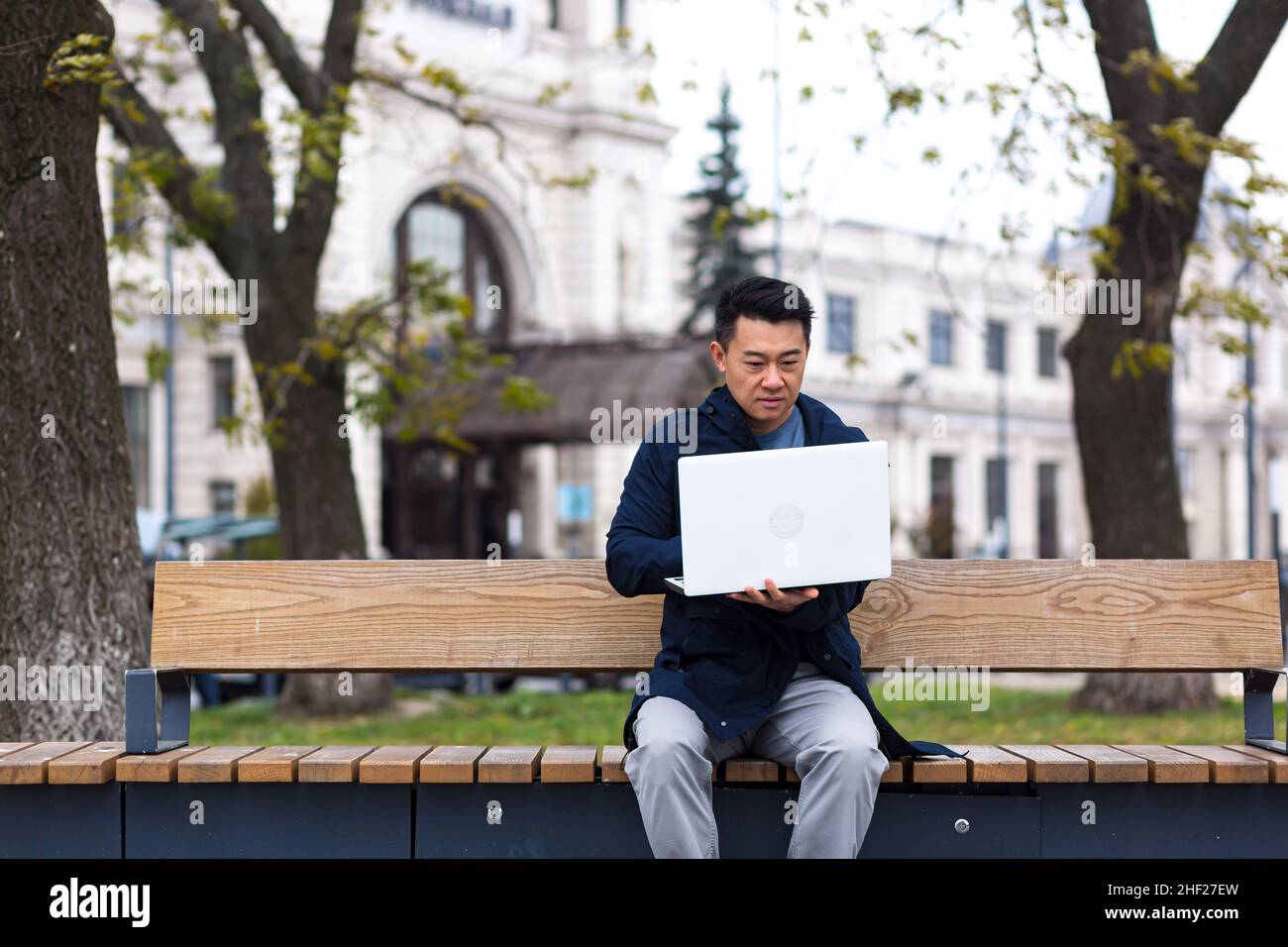 uomo d'affari cinese che lavora in linea a distanza sul laptop, uomo asiatico fuori ufficio Foto Stock