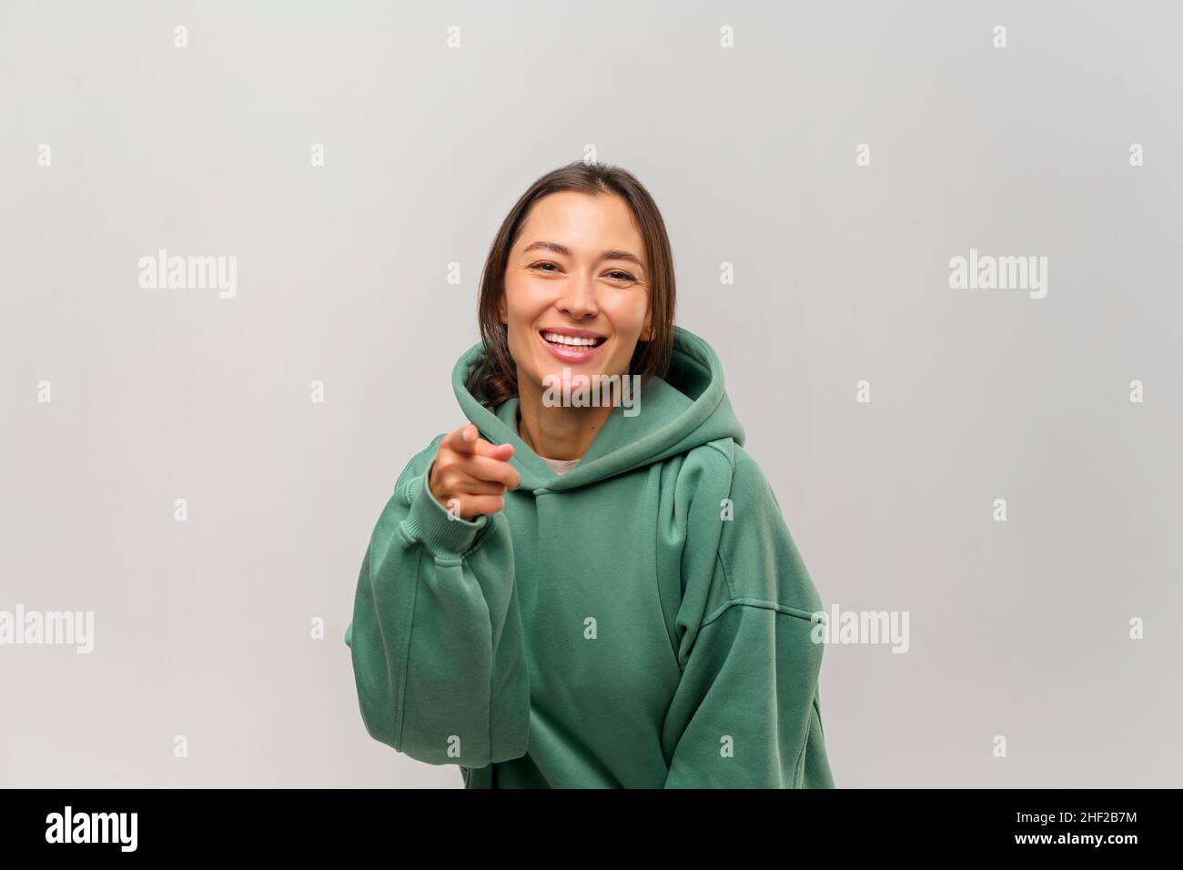 Donna felice soddisfatto con capelli marroni puntando le dita su di voi guardando la macchina fotografica con un sorriso toothy, congratulandosi con la vittoria. Studio interno girato isolato su sfondo bianco Foto Stock