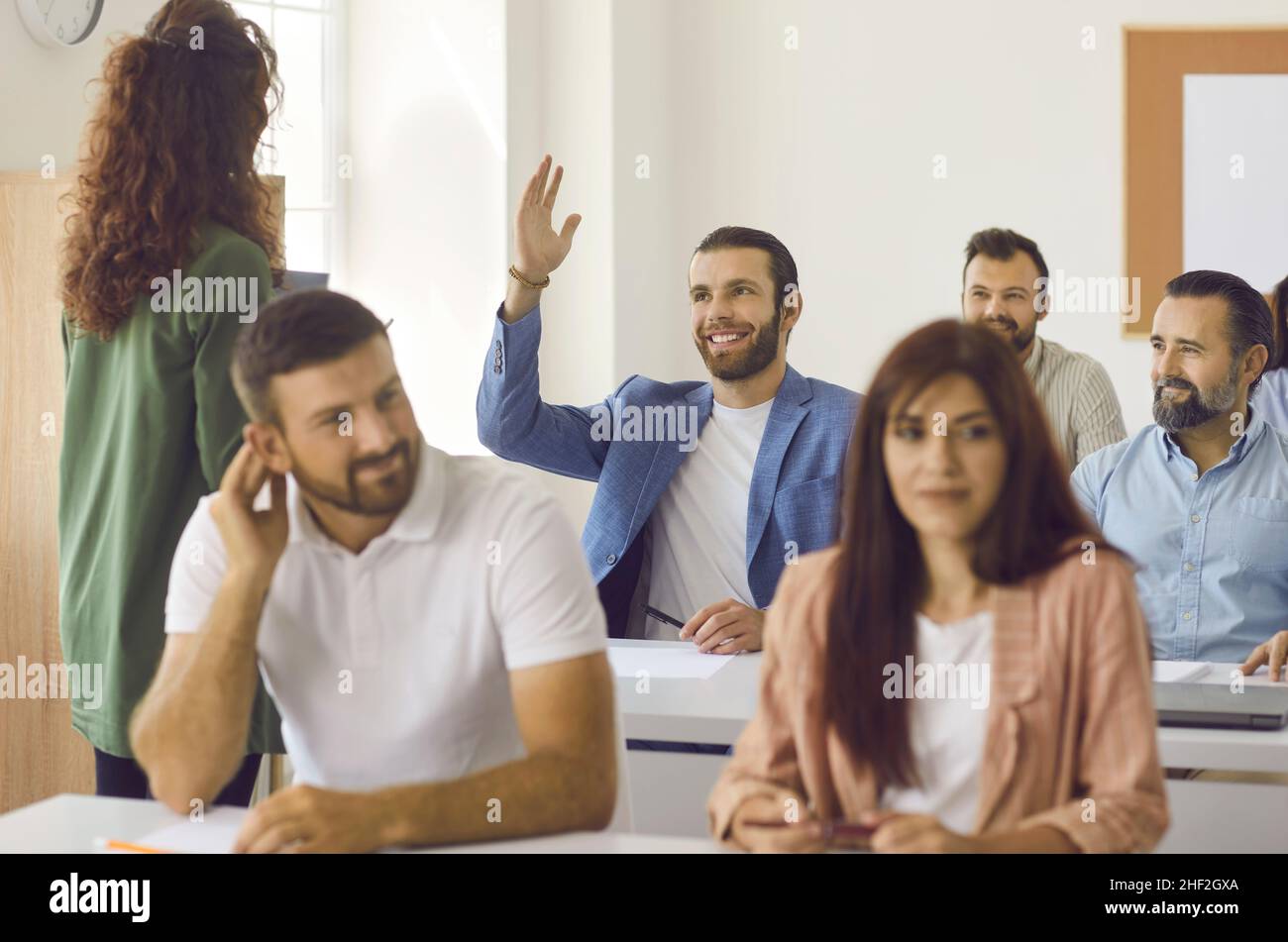 L'uomo solleva la mano per porre all'insegnante una domanda durante una classe di formazione aziendale Foto Stock