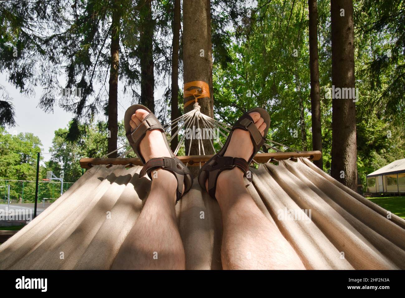 Piedi maschi in sandali su amaca. Uomo che riposa sull'amaca durante la giornata estiva nel parco. Relax e vacanza concetto. Foto Stock