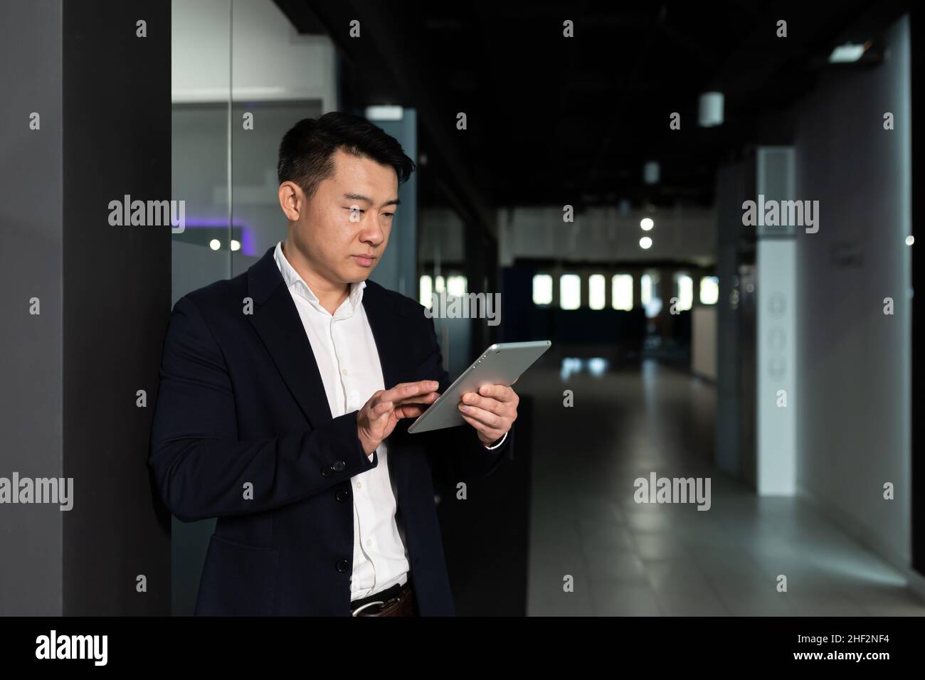 Serio lavoratore maschile asiatico si è concentrato sul lavoro di lavoro con computer tablet in un ufficio moderno Foto Stock