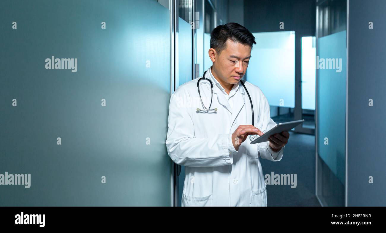 Medico asiatico serio, usa un computer tablet, l'uomo lavora in una clinica moderna Foto Stock