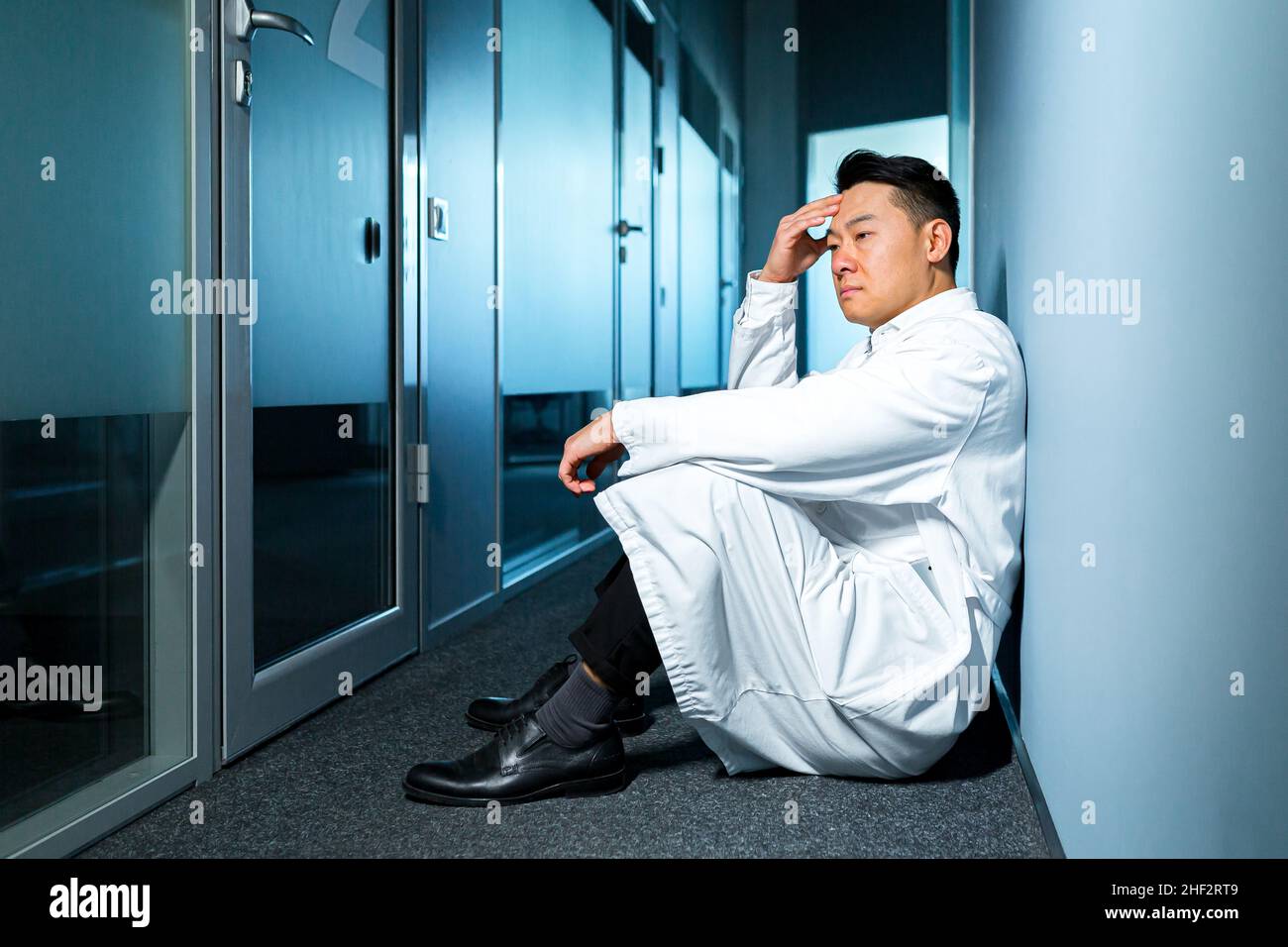Turbato e pensiero asiatico uomo seduto sul pavimento in laboratorio, scienziato frustrato Foto Stock