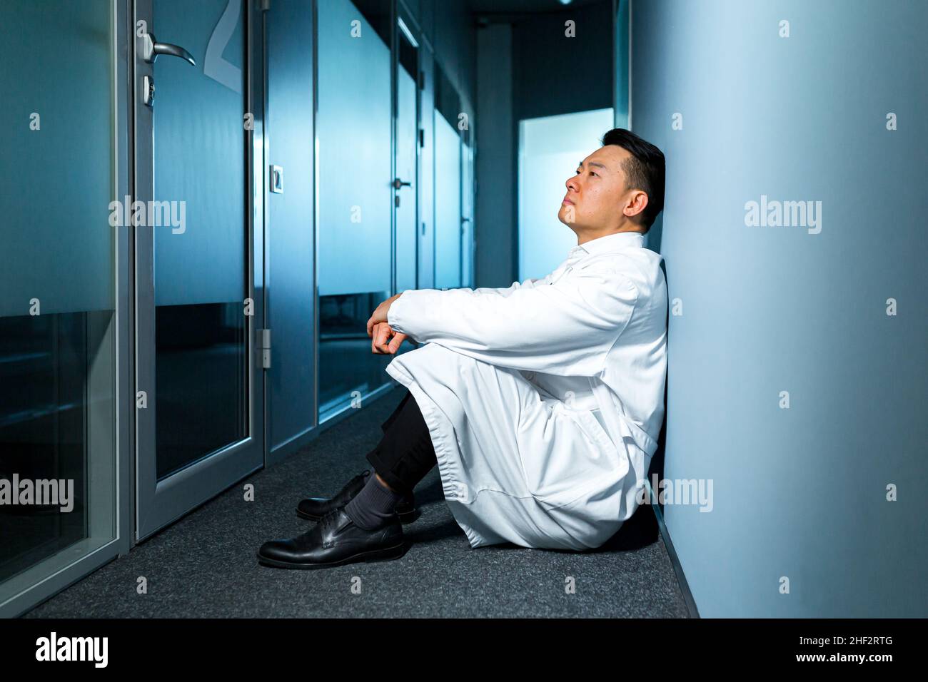 Turbato e pensiero asiatico uomo seduto sul pavimento in laboratorio, scienziato frustrato Foto Stock