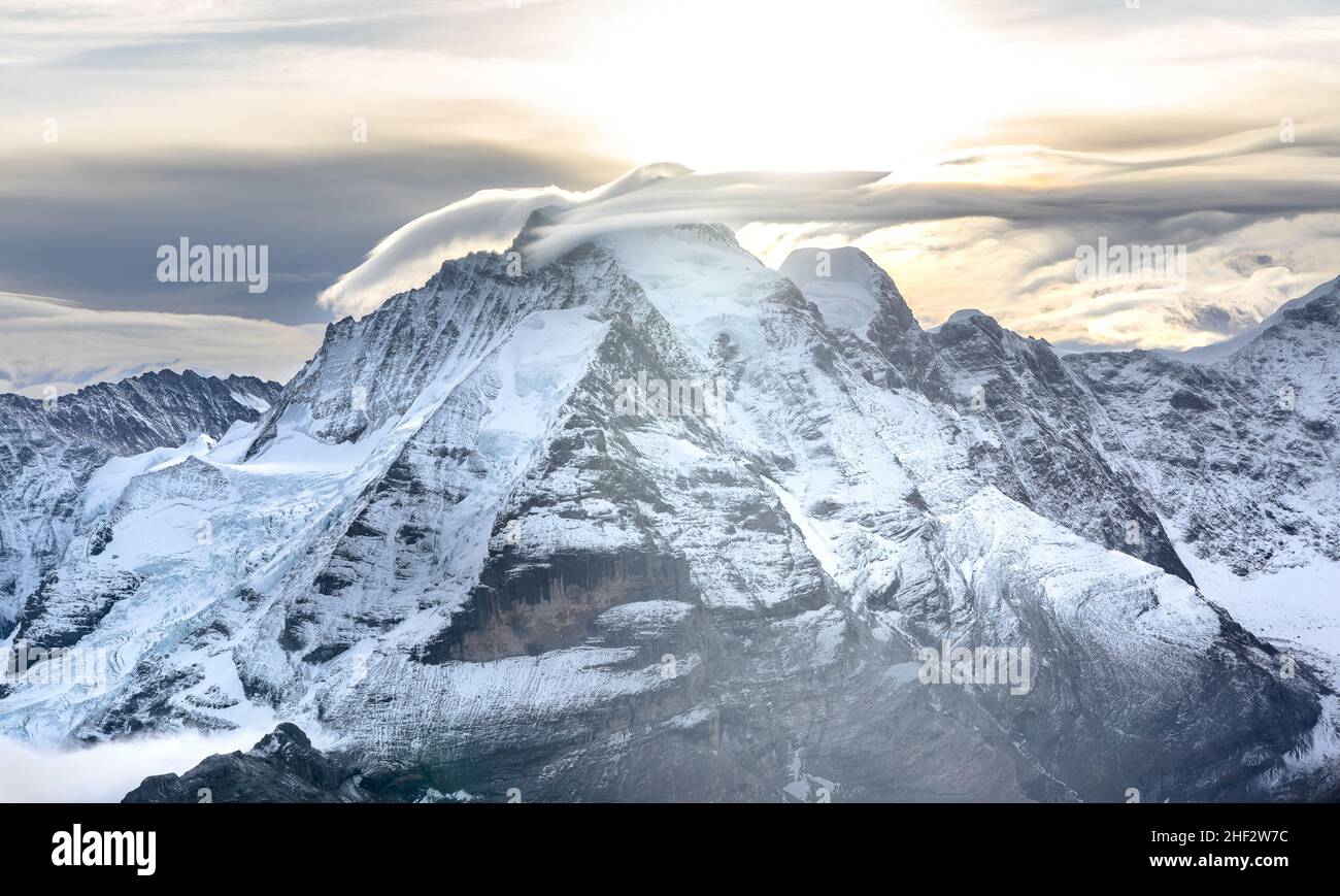 Vista delle famose vette Jungfrau, Mönch ed Eiger dalla montagna Schilthorn nelle Alpi svizzere in Svizzera all'alba con le nubi e le volpi drammatiche Foto Stock