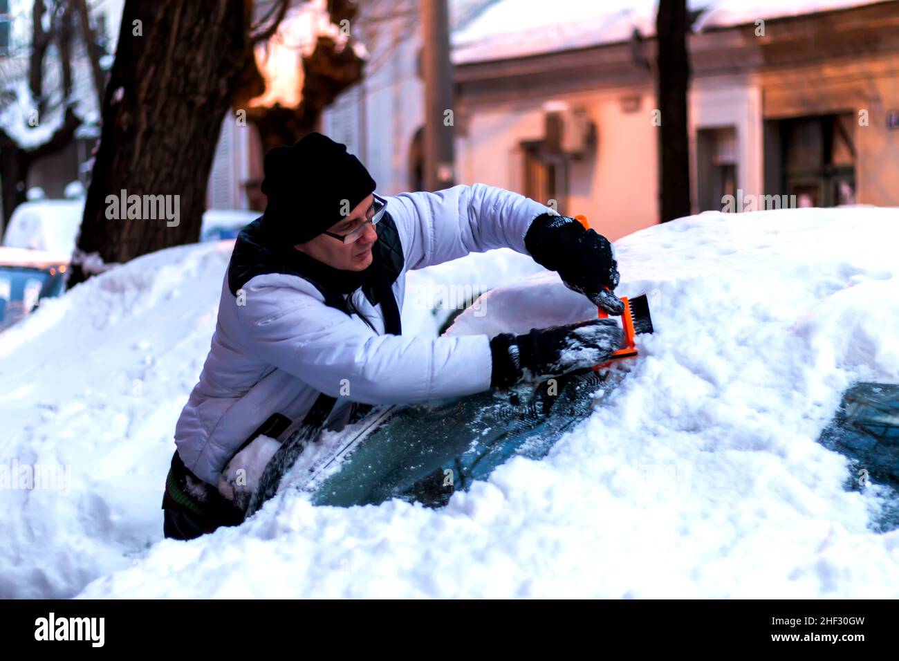 Uomo che pulisce il parabrezza dell'auto con raschietto e spazzola dalla neve e dal ghiaccio Foto Stock