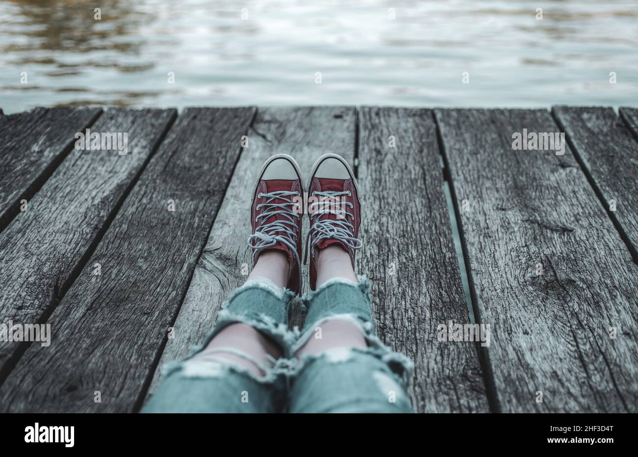 Il bambino in sneakers rosse sta riposando in un campo per bambini. Adolescente in sneakers con una vista sul lago fuori della città. Vacanza spensierata durante il Foto Stock