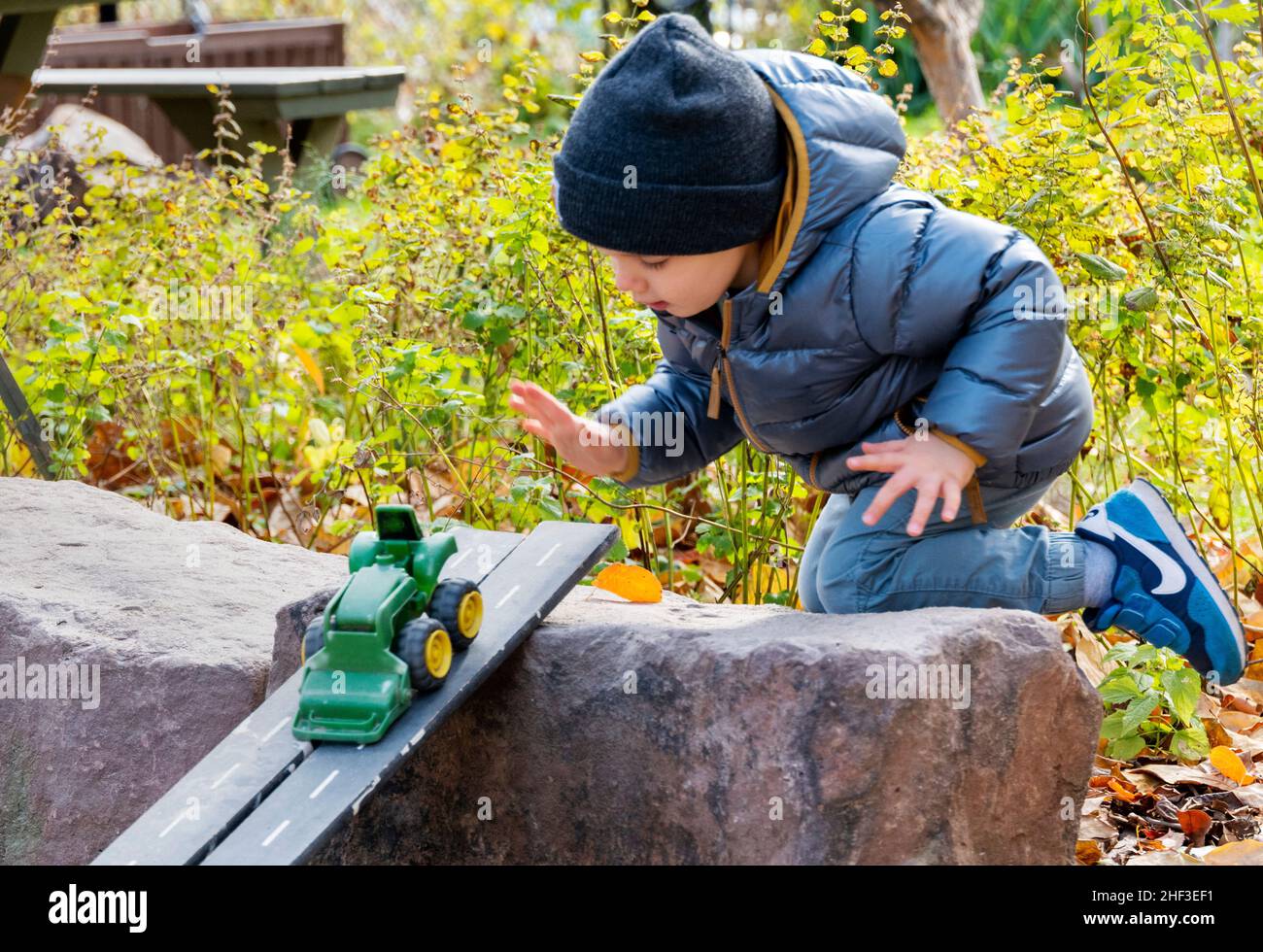 Ragazzo di due anni che gioca con il trattore giocattolo sulla rampa in sandbox parco città Foto Stock