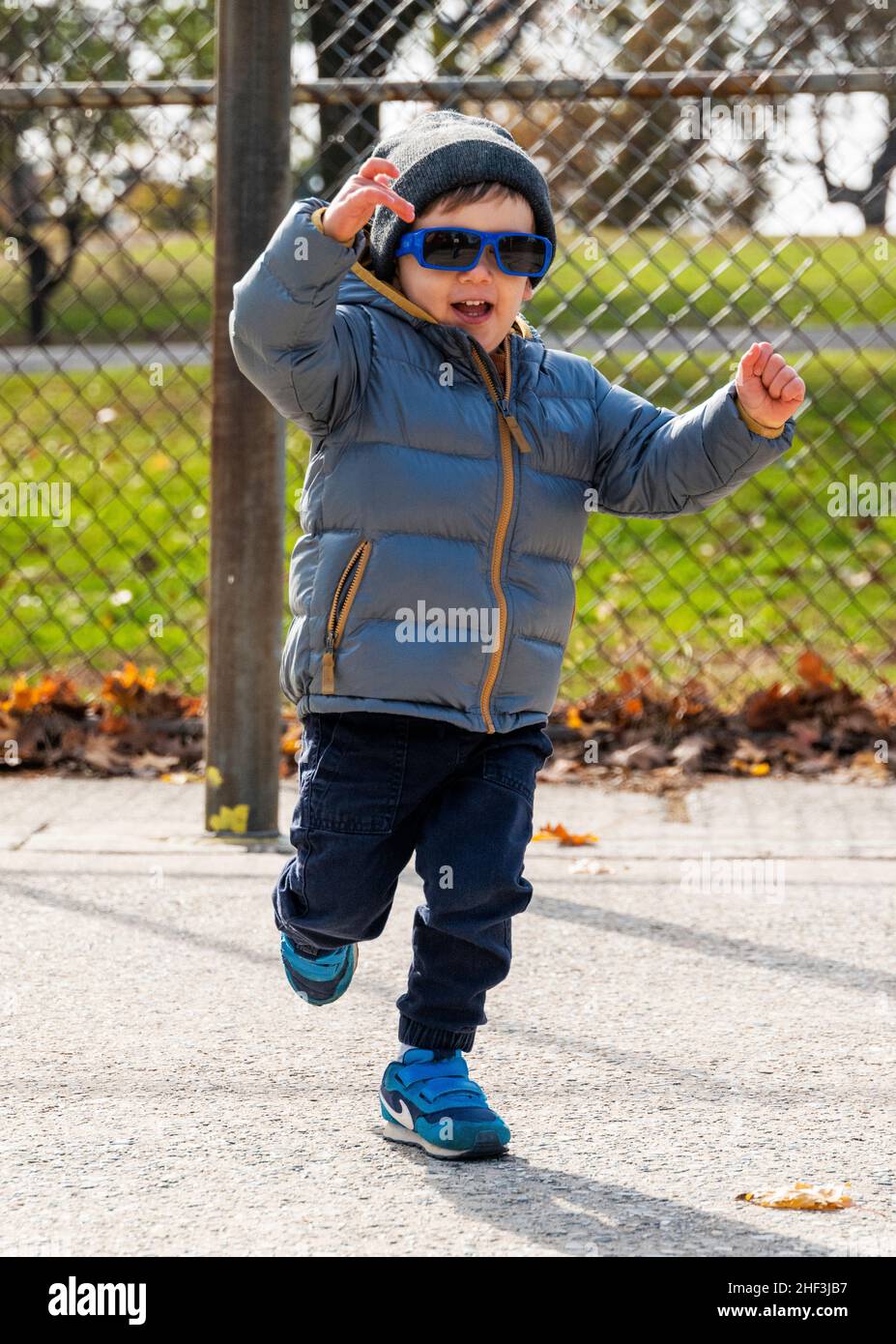 Ragazzo di due anni con occhiali da sole in esecuzione sul parco giochi della città; Corinthian Gardens; Philadelphia; Pennsylvania; USA Foto Stock
