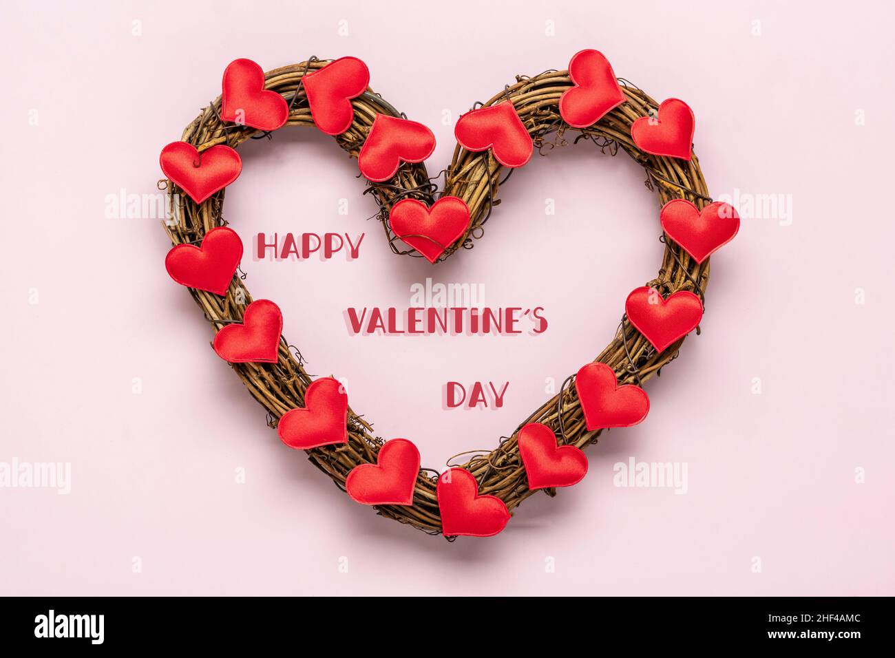 Corona di rattan a forma di cuore decorata con cuori rossi su sfondo rosa Vista dall'alto Flat Lay Holiday Card buon San Valentino, amore concetto Copia spazio. Foto Stock
