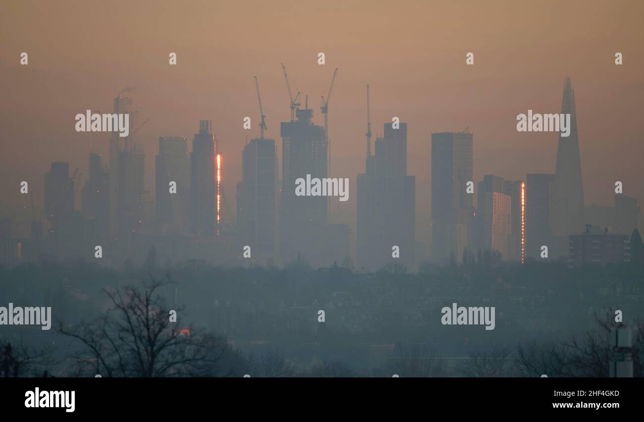 Wimbledon, Londra, Regno Unito. 14 gennaio 2022. La luce del sole dell'alba colpisce il bordo della St George Wharf Tower, a sinistra, a Vauxhall attraverso la nebbia mattutina in un giorno in cui l'allarme alto livello di inquinamento atmosferico si spegne. Credit: Malcolm Park/Alamy Live News Foto Stock