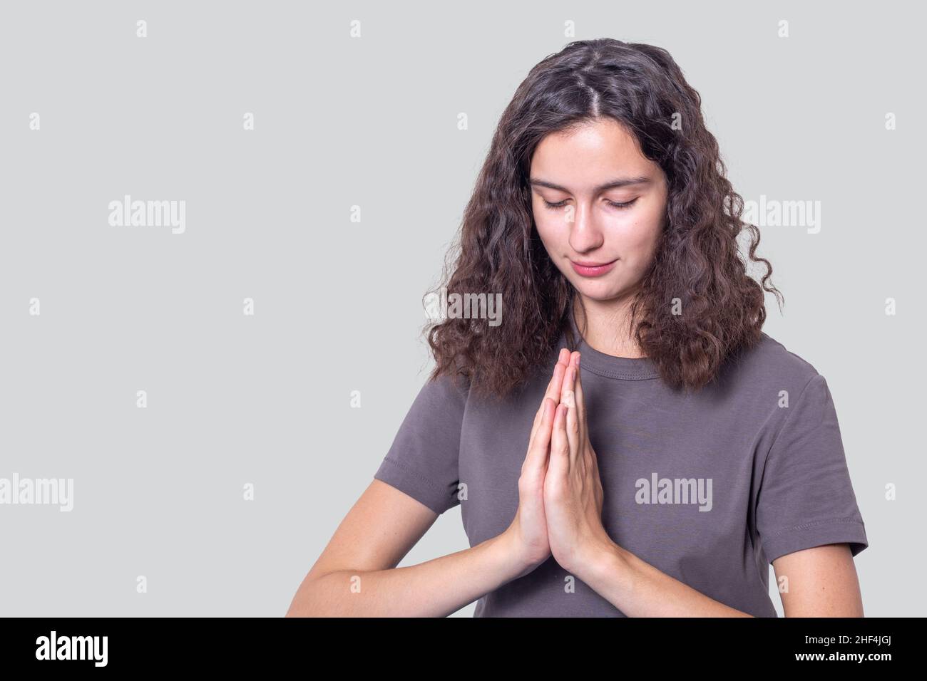 Ritratto di una ragazza speranzosa con capelli ricci tiene le mani insieme in un gesto di preghiera. Rendere omaggio, adorare il Buddha, salutare, esprimere un apolo Foto Stock