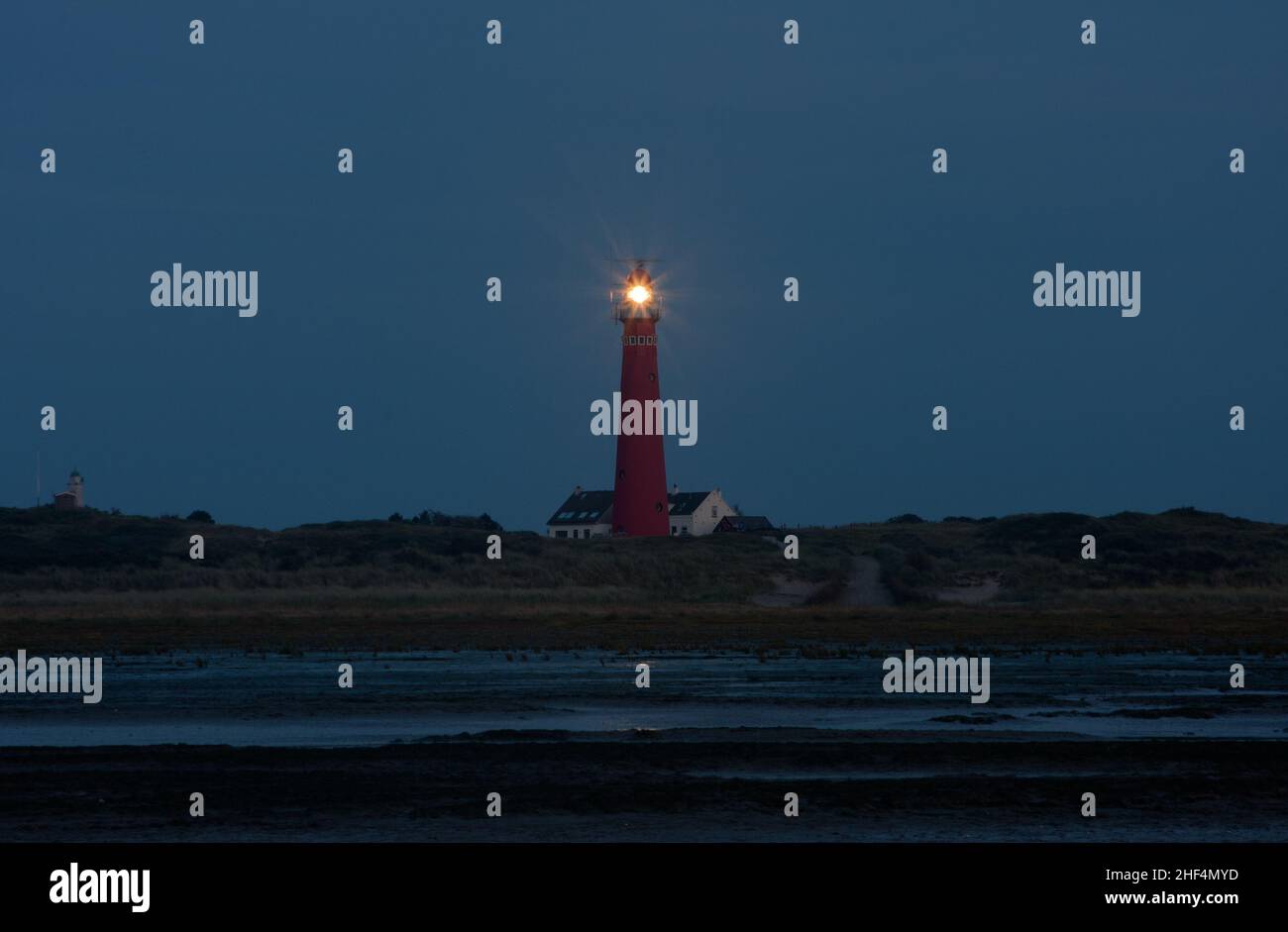 Vista sulla spiaggia di notte sul faro dell'isola olandese di Schiermonnikoog, accanto alla casa bianca del guardiano del faro Foto Stock