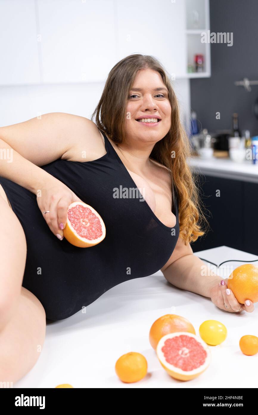 Costume da bagno femminile modello Plus in nero in posa sul tavolo da cucina con agrumi, arancio, pompelmo, mandarino. Cibo sano, corpo positivo. Primo piano. Foto di alta qualità Foto Stock