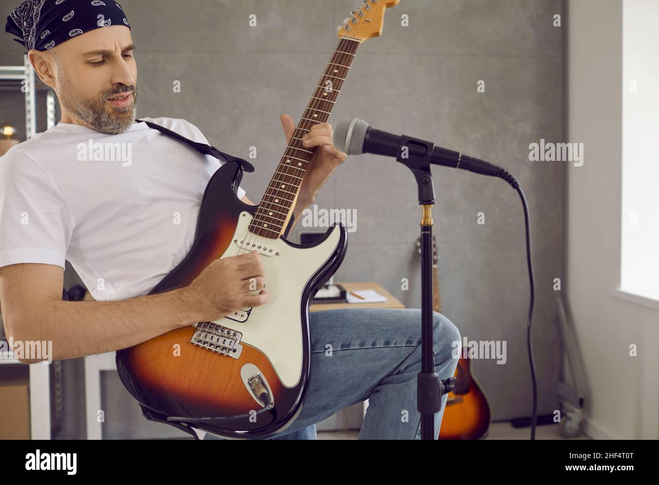 Chitarrista maschile suona riff sulla sua chitarra elettrica in studio moderno con microfono Foto Stock