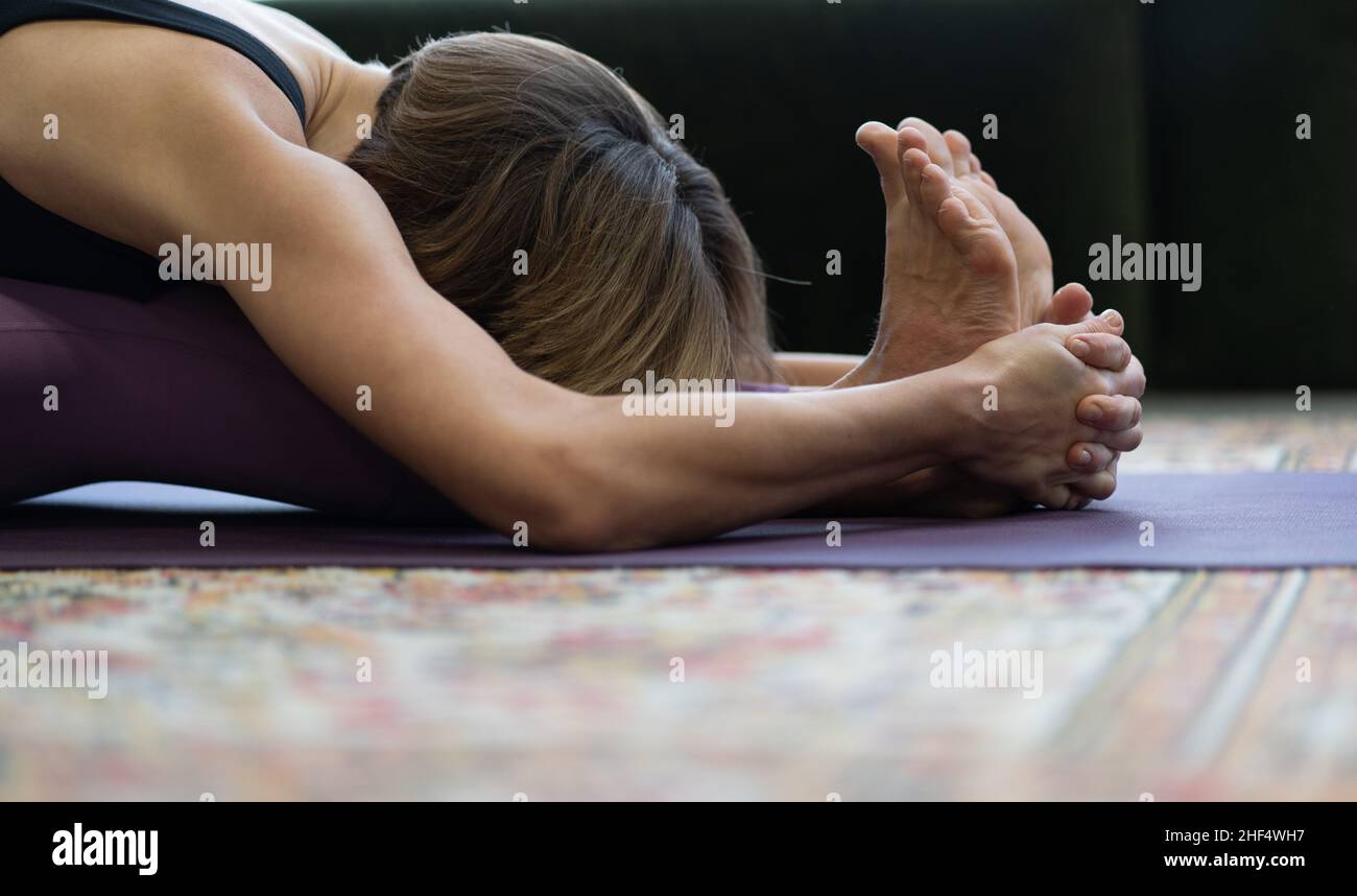Donna Practices Yoga Asanas al mattino per l'energia per l'intera giornata. Yoga Signora che fa seduta piega avanti esercizio faccia in giù.primo piano. Foto Stock