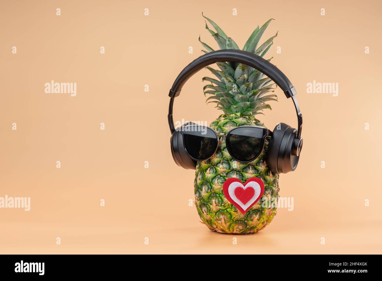 L'idea degli amanti per San Valentino nell'immagine di un ananas indossando cuffie e occhiali da sole. Su sfondo giallo. Foto Stock