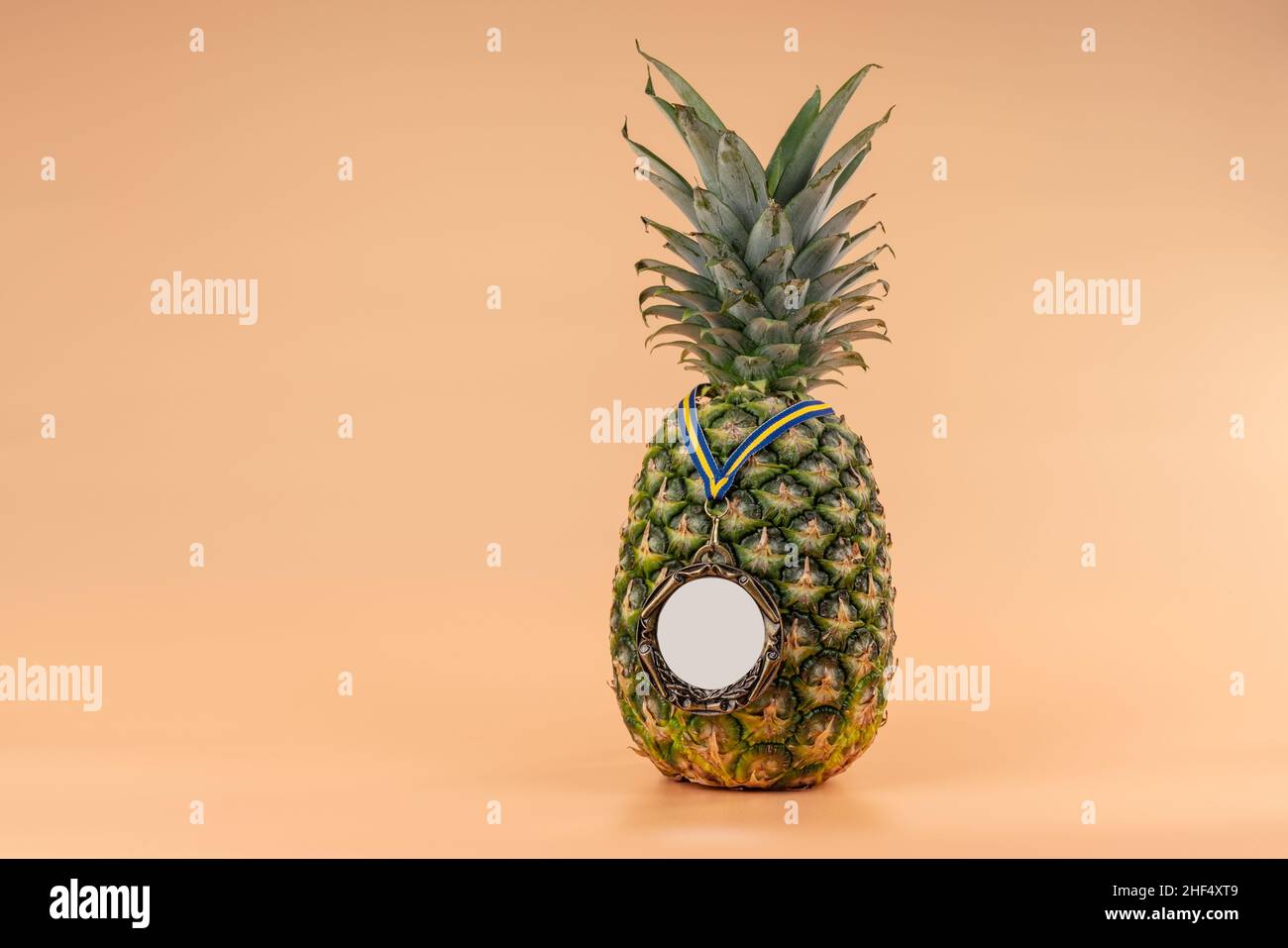 Interpretazione del frutto dell'ananas in un'immagine umana con una medaglia come simbolo di vittoria, successo e forza. Su sfondo giallo. Foto Stock