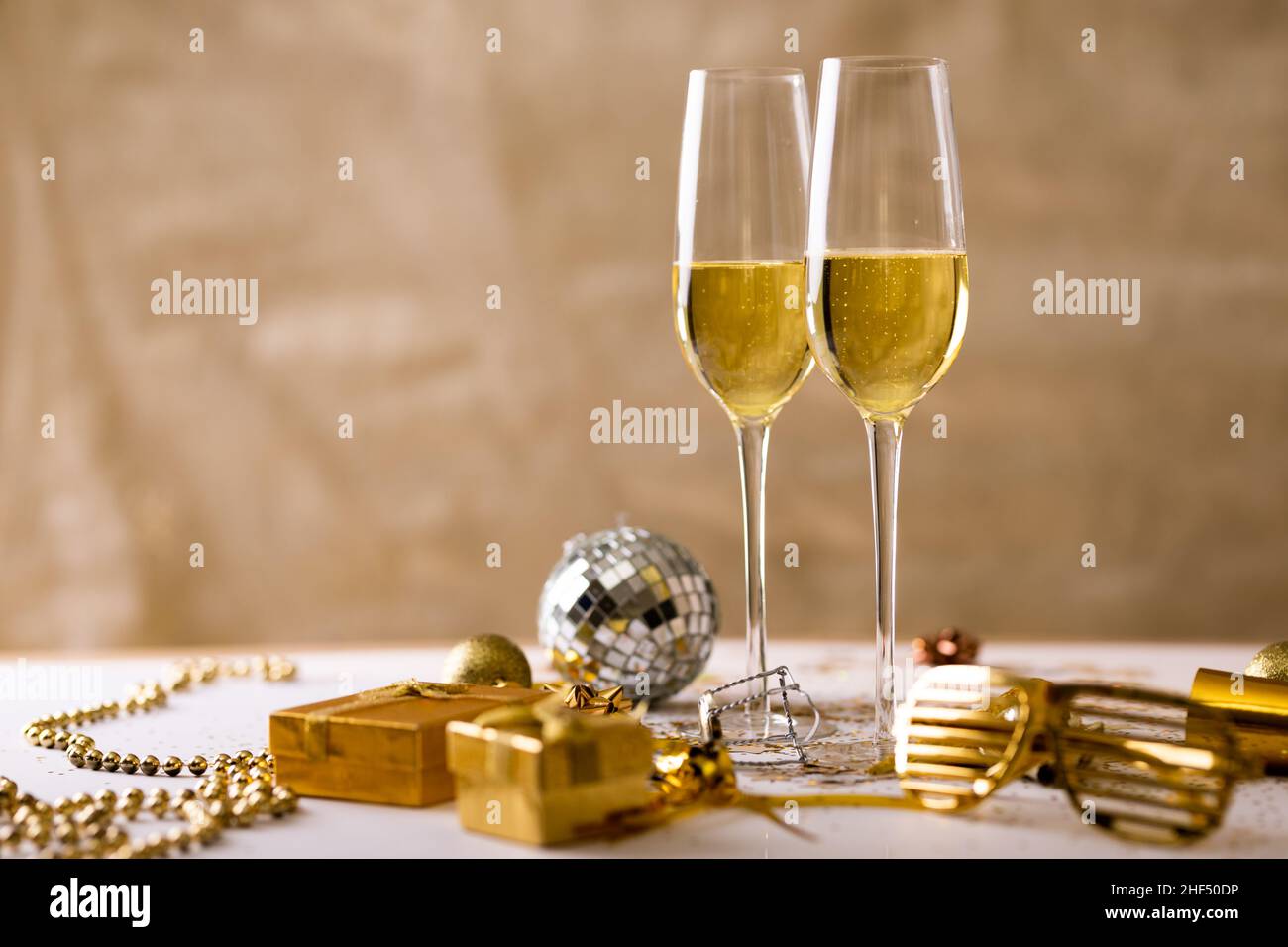 Flute di champagne con decorazione color oro e scatole regalo su sfondo beige, spazio copia Foto Stock