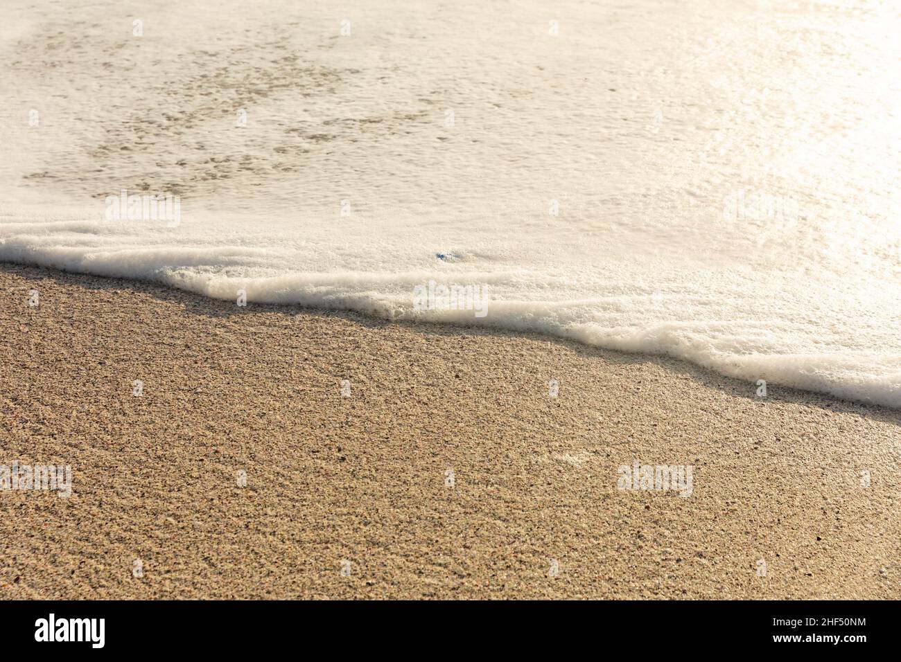 Vista ad alto angolo della schiuma bianca dell'onda di mare sulla riva della spiaggia soleggiata Foto Stock