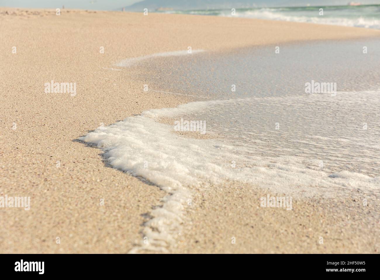 Vista ad alto angolo della schiuma bianca dell'onda di mare sulla riva della spiaggia soleggiata Foto Stock