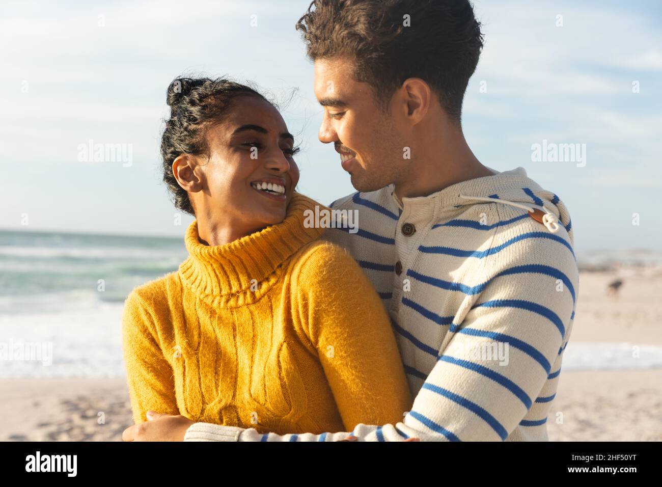 Sorridendo coppia biraciale che si guardano l'un l'altro mentre si gode di una giornata di sole sulla spiaggia Foto Stock