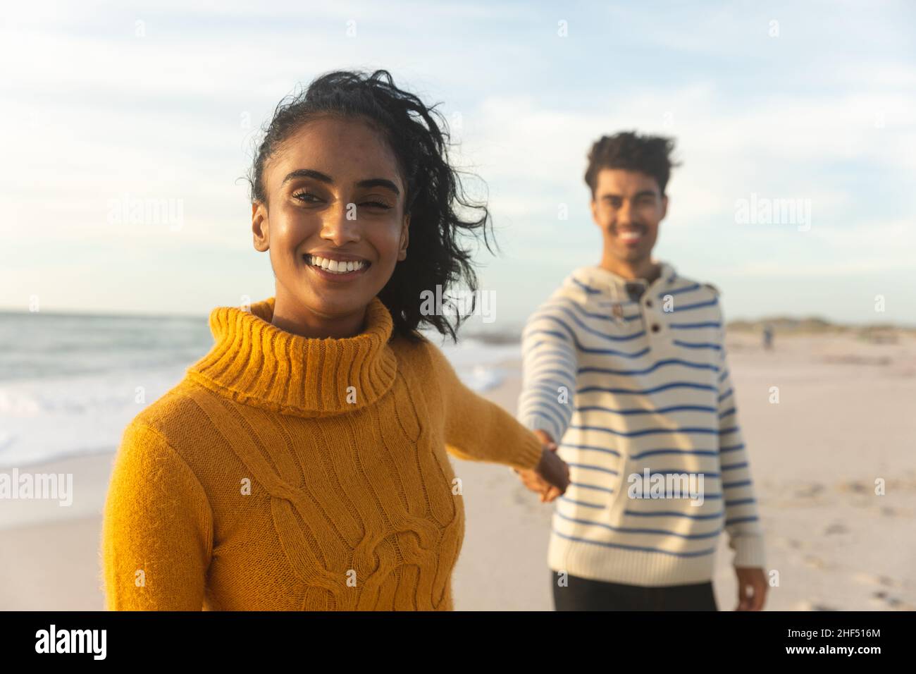 Ritratto di giovane donna biraciale sorridente che tiene la mano con il ragazzo in piedi dietro di lei in spiaggia Foto Stock