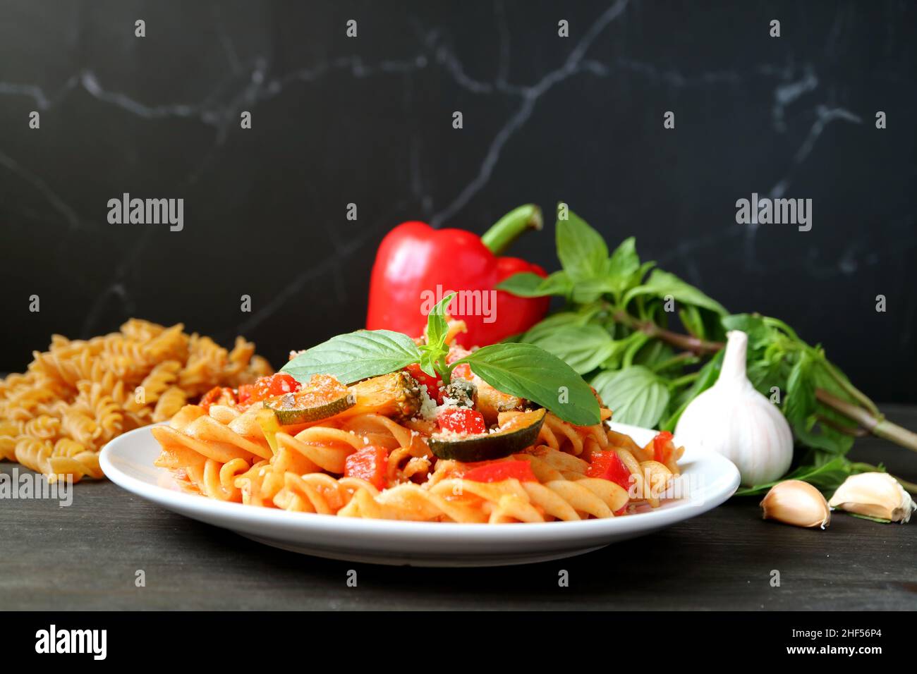 Gustosa e salutare pasta di Fusilli integrale in salsa di pomodoro con ingredienti freschi sullo sfondo Foto Stock