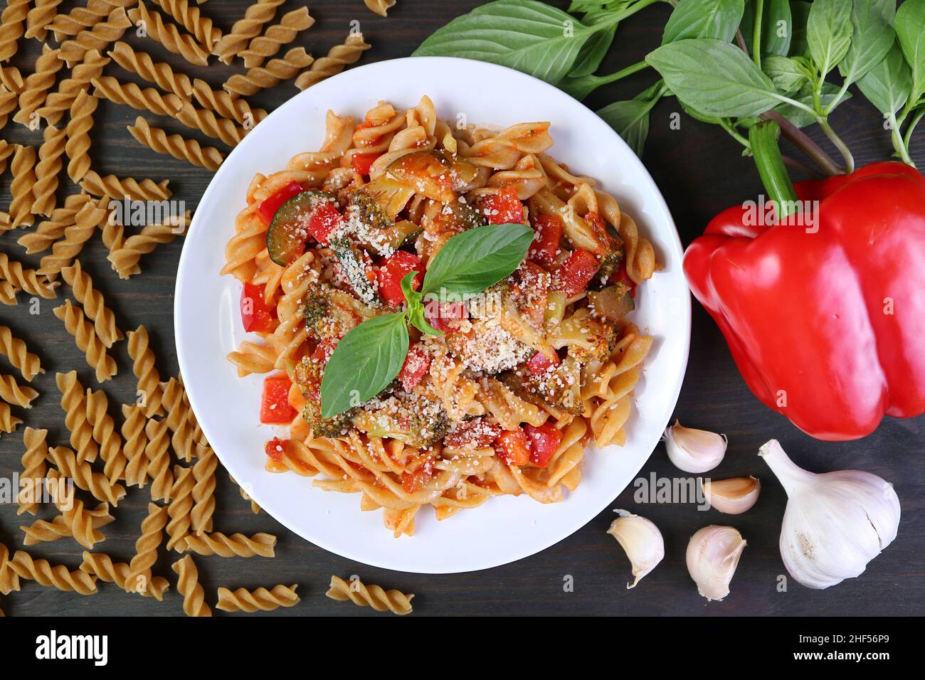Piatto di deliziosa pasta di Fusilli di frumento intero in salsa di pomodoro con i suoi ingredienti sparsi intorno Foto Stock