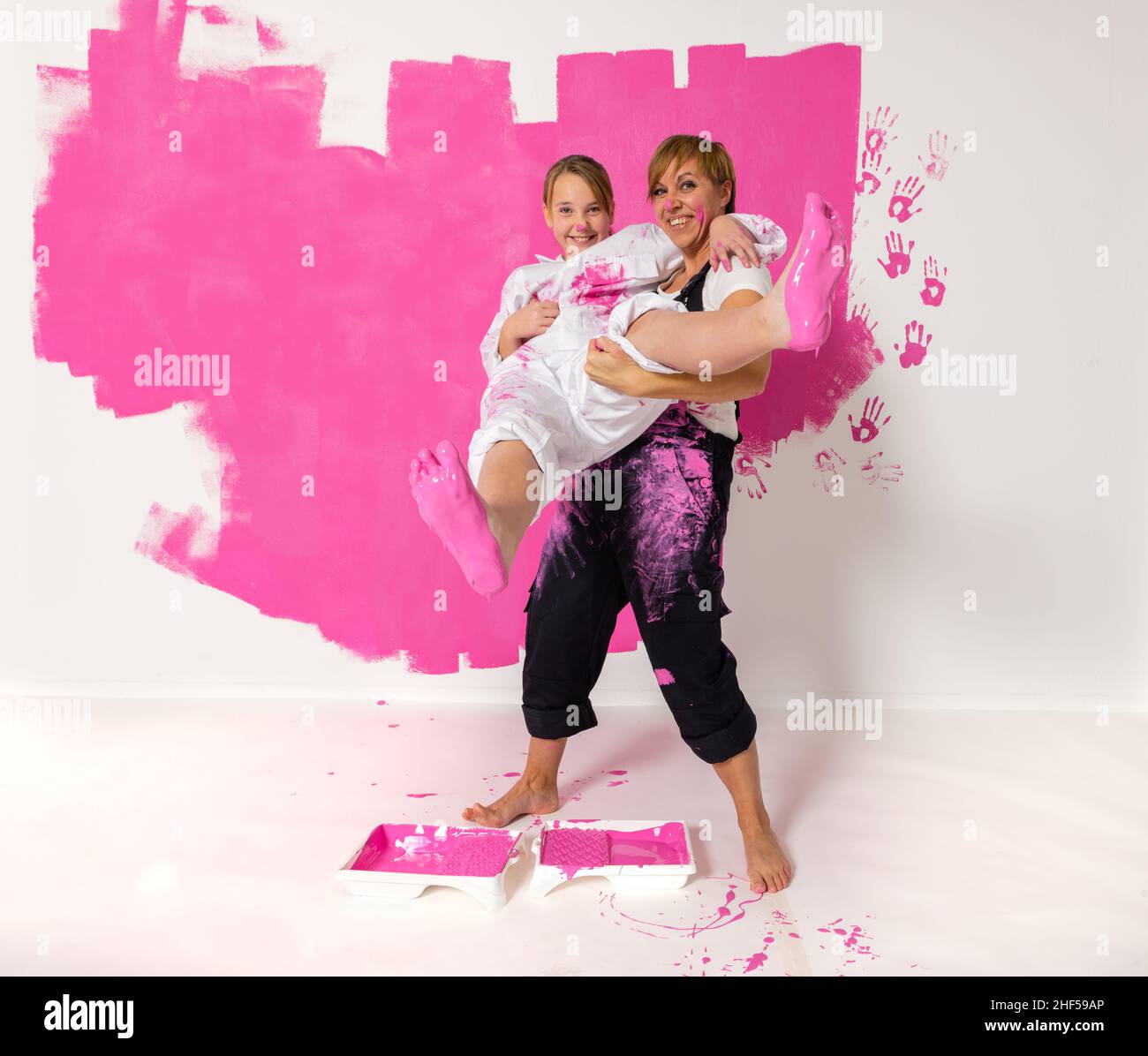 Madre e figlia in piedi di fronte ad un muro dipinto con color.Mother rosa sta tenendo la ragazza e la ragazza ha colore su entrambi i piedi. Entrambi sono w Foto Stock