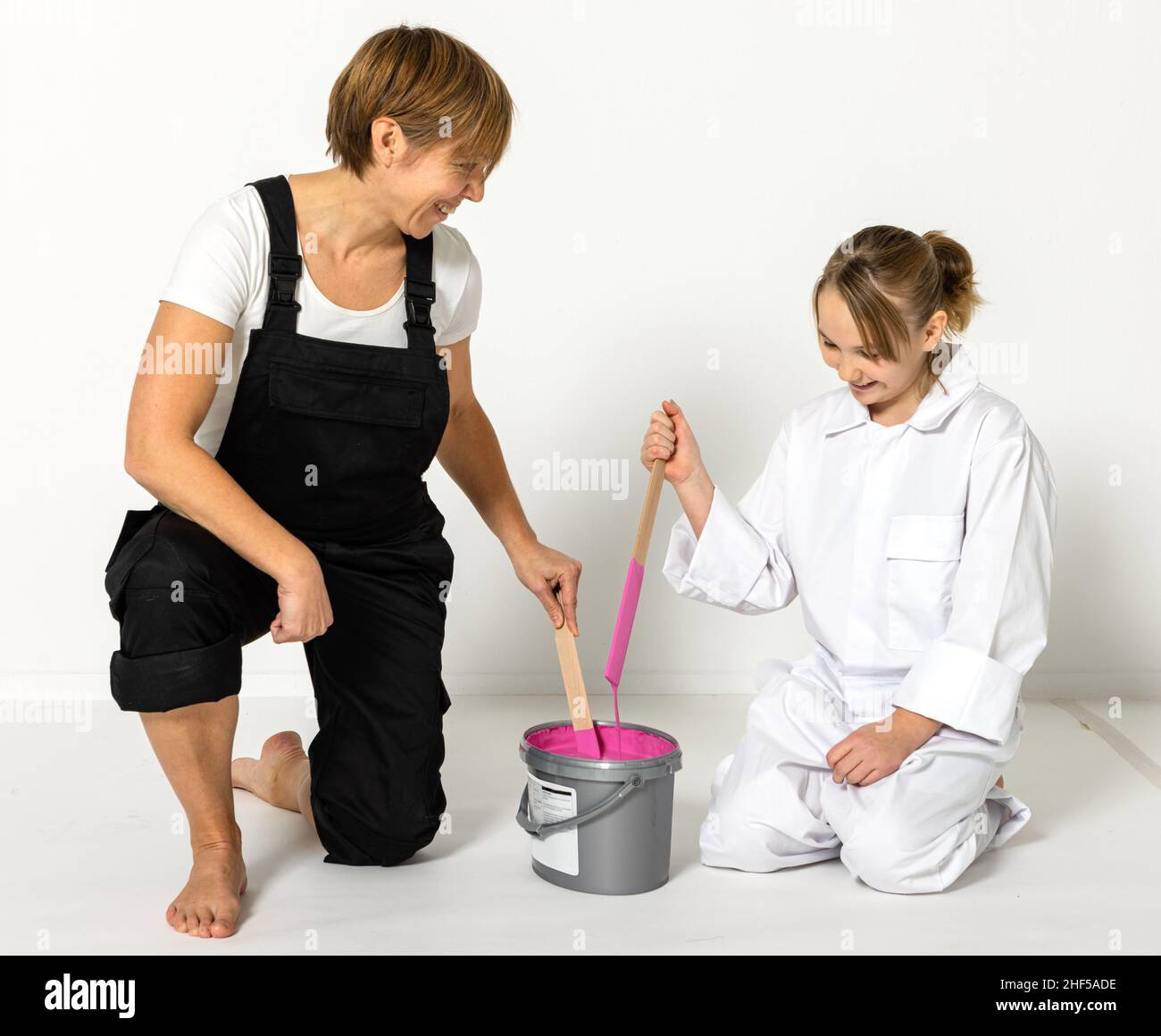 Madre e figlia che si preparano a dipingere a casa. Stanno mescolando il colore rosa con i bastoni. Foto Stock