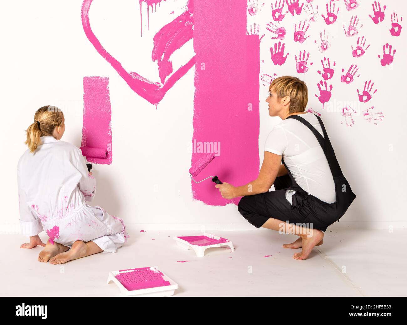 Madre e figlia sta dipingendo con vernice rosa su una parete bianca. Entrambi sono seduti. Foto Stock