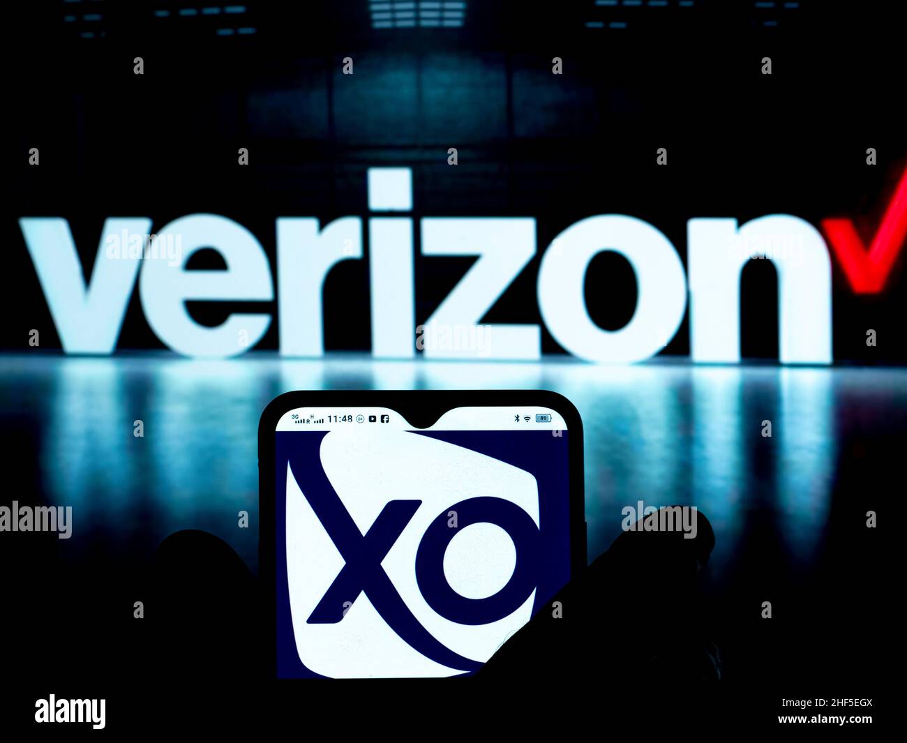 In questa foto, XO Communications, un'azienda di proprietà del logo Verizon visualizzata su uno smartphone con il logo Verizon sullo sfondo. Foto Stock