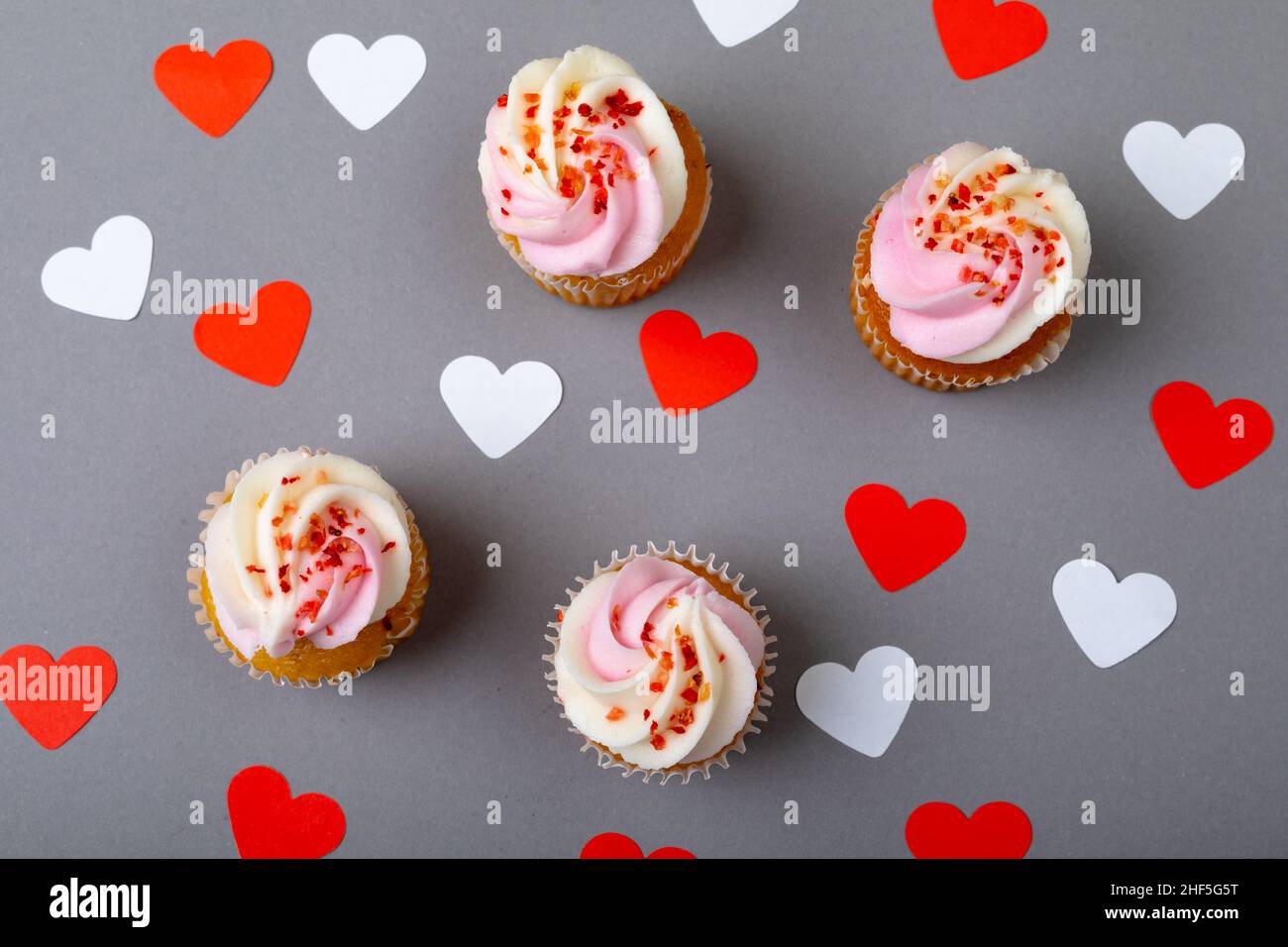 Spruzzatori su cupcake freschi un cuore rosso e bianco forma su sfondo grigio Foto Stock