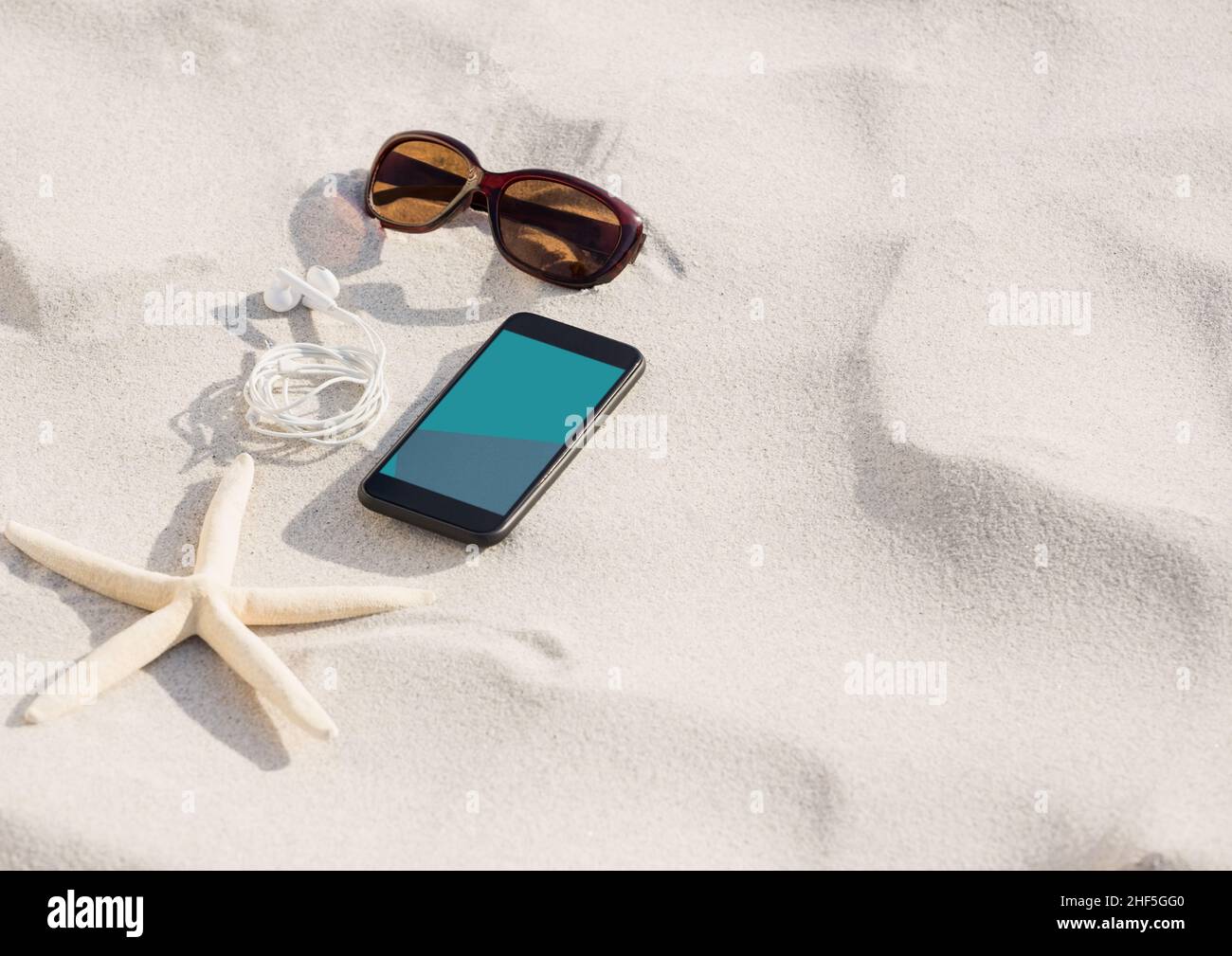 Smartphone, occhiali da sole, auricolari e pesci stella sulla sabbia in spiaggia con spazio copia Foto Stock