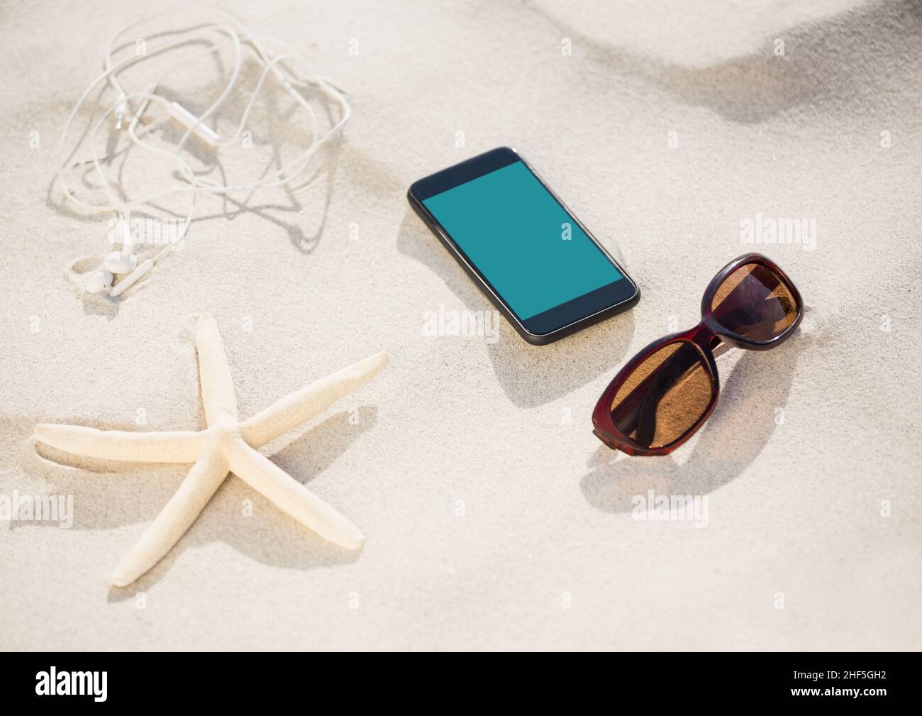 Smartphone, occhiali da sole, auricolari e pesci stella sulla sabbia in spiaggia con spazio copia Foto Stock