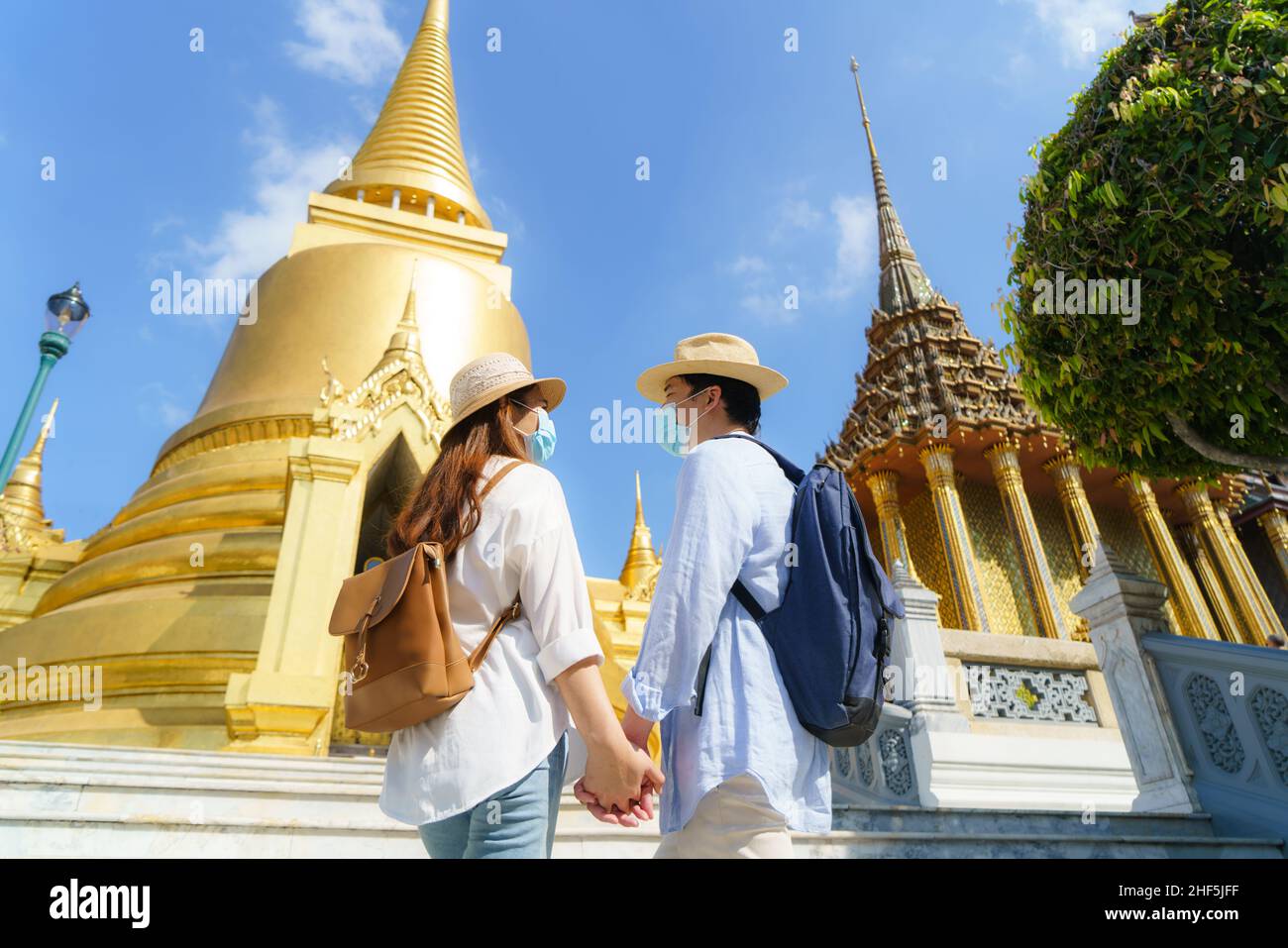 Coppie asiatiche turisti felici di viaggiare indossando maschera per proteggere da Covid-19 in loro vacanze nel tempio Wat Phra Kaew a Bangkok, Thailandia Foto Stock