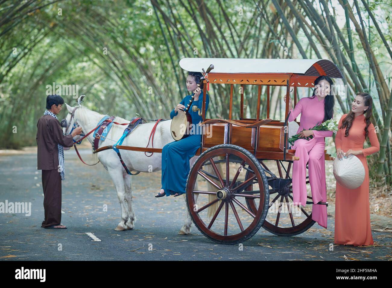 Ho Chi Minh City, Viet Nam: Le ragazze vietnamite indossano ao dai bianco e cavalcano su una carrozza trainata da cavalli su una strada di campagna in Vietnam Foto Stock