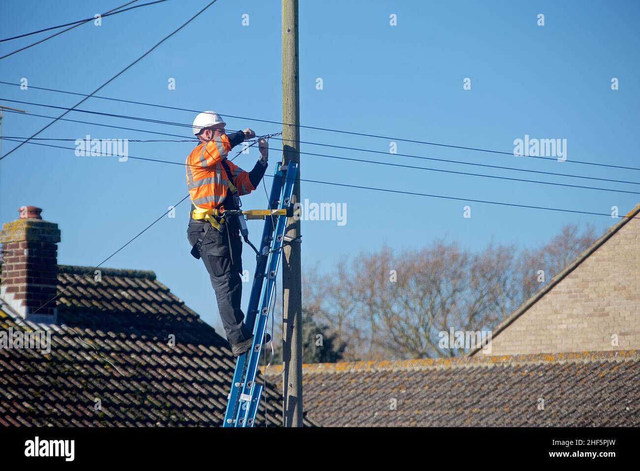 Ingegnere di telecomunicazioni a portata aperta al lavoro su una scala, indossa i DPI corretti per il lavoro in corso, rispettando al contempo le normative H&S. Foto Stock