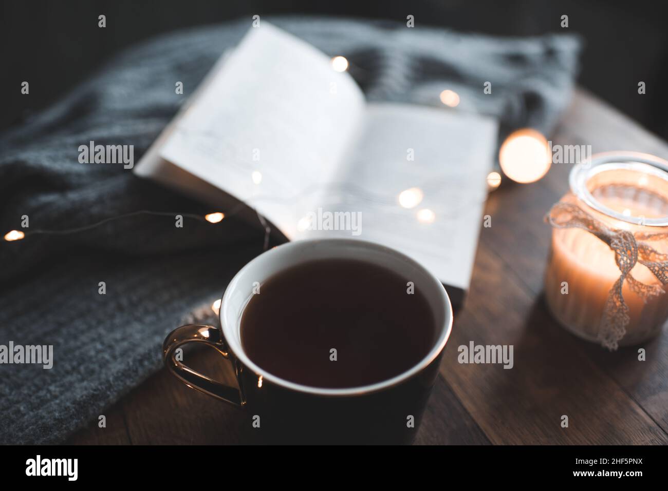 Tazza di caffè di resh balck con libro di carta aperto e candela che brucia sullo sfondo sopra le luci di bagliore si avvicinano. Buongiorno. Foto Stock