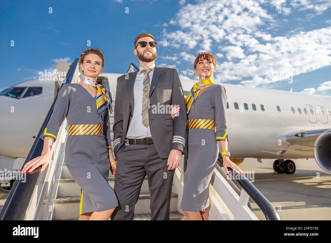 Capitano dell'aviazione maschile e due assistenti di volo donne in piedi sulle scale di imbarco aereo e sorridenti Foto Stock