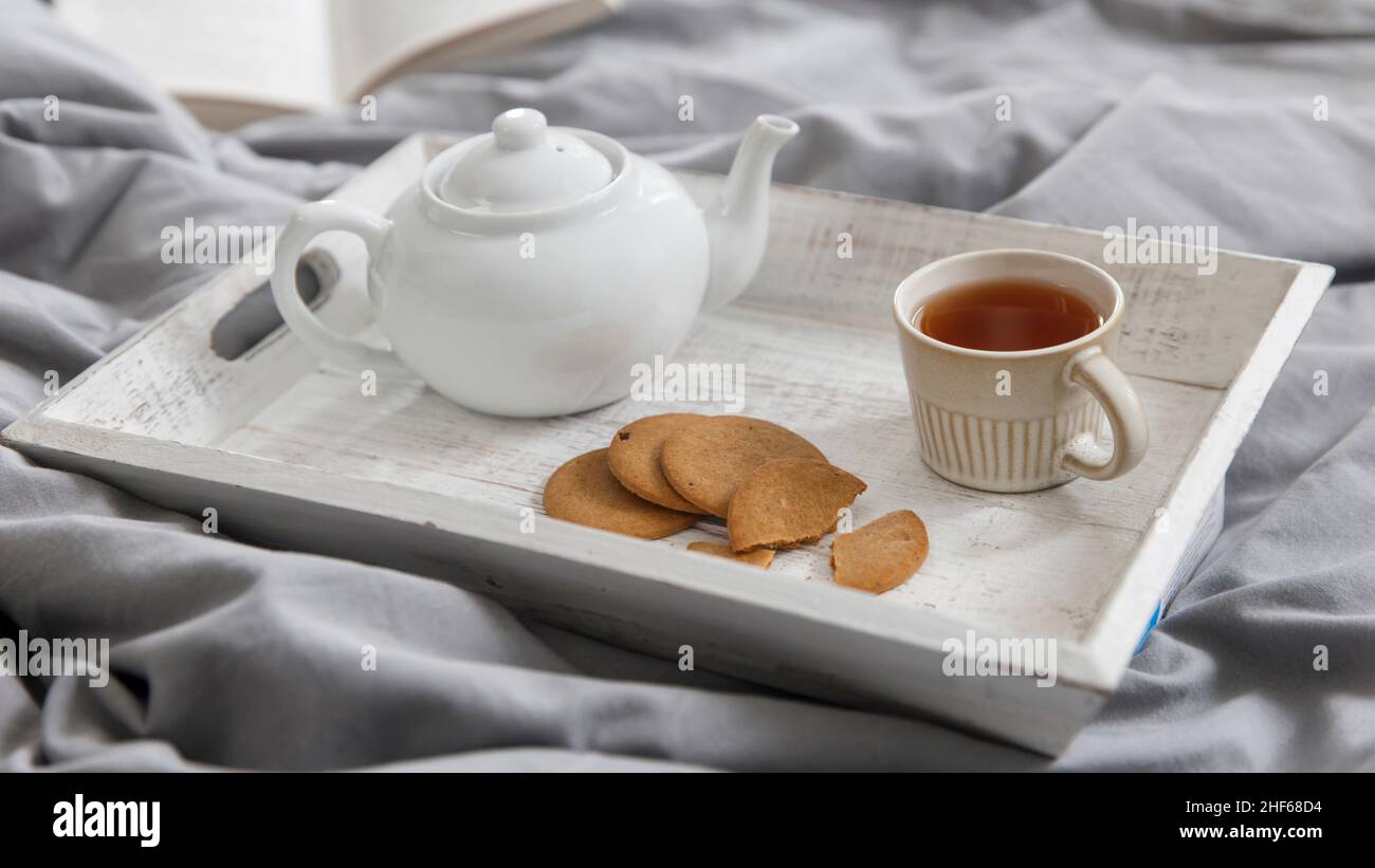 concetto di coziness interno e domestico. Vista dall'alto. Una tazza di tè, una teiera con tè alle erbe, una ciotola di zucchero su un vassoio di legno sul letto. Tazza in porcellana Foto Stock