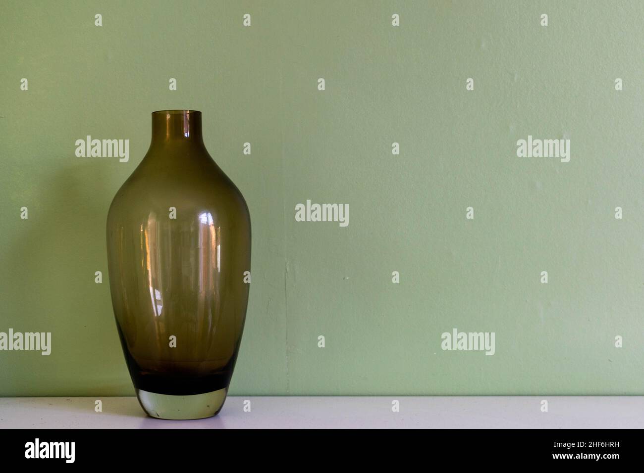 Decorazioni minimaliste per la casa e un'idea di stile di vita. Tranquillo vaso di vetro trasparente su una mensola bianca su sfondo verde chiaro. Decorazioni e ornamenti per la casa Foto Stock