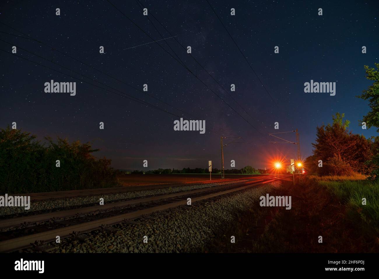 Milkyway con il suo centro galattico su una pista ferroviaria solitaria che si erge sopra il segnale di fermata del treno in una notte stellata Foto Stock
