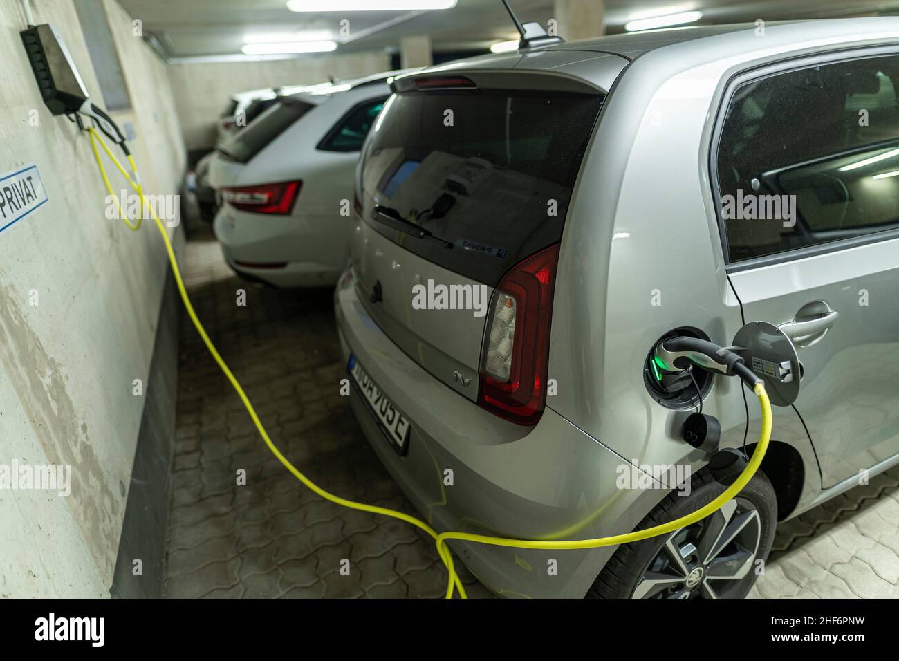 Collegato in filo di carica a un'auto elettrica in un garage di carico domestico con altre auto. Scena autentica del nuovo processo di rifornimento dell'auto a casa invece di andare alla stazione di servizio successiva Foto Stock
