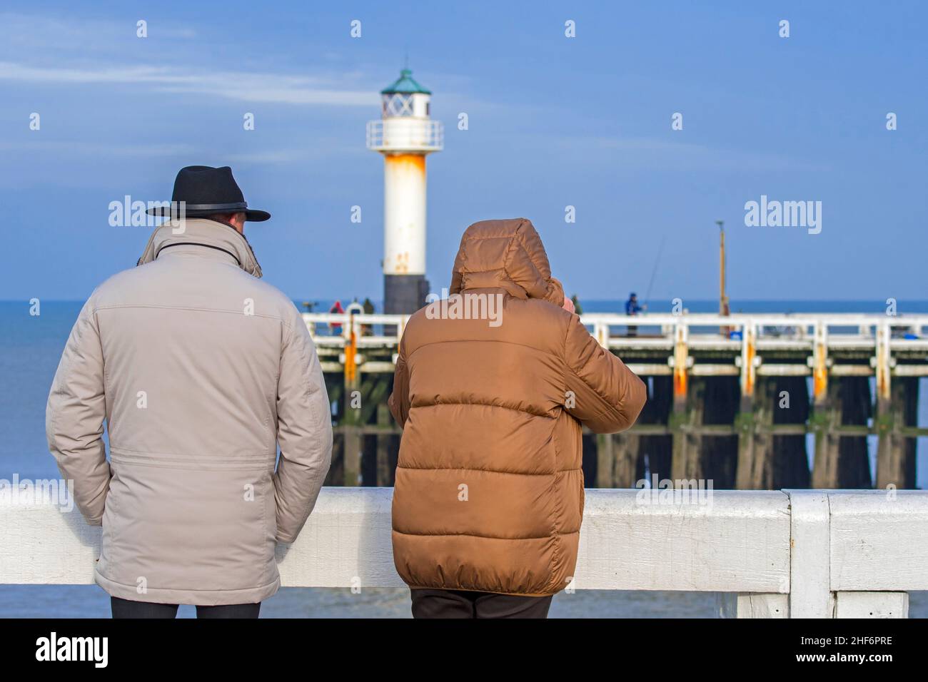 Coppia anziana vestita con cappotti caldi sul molo di legno all'ingresso del porto di Nieuwpoort / Nieuport lungo la costa belga del Mare del Nord in inverno, Wes Foto Stock